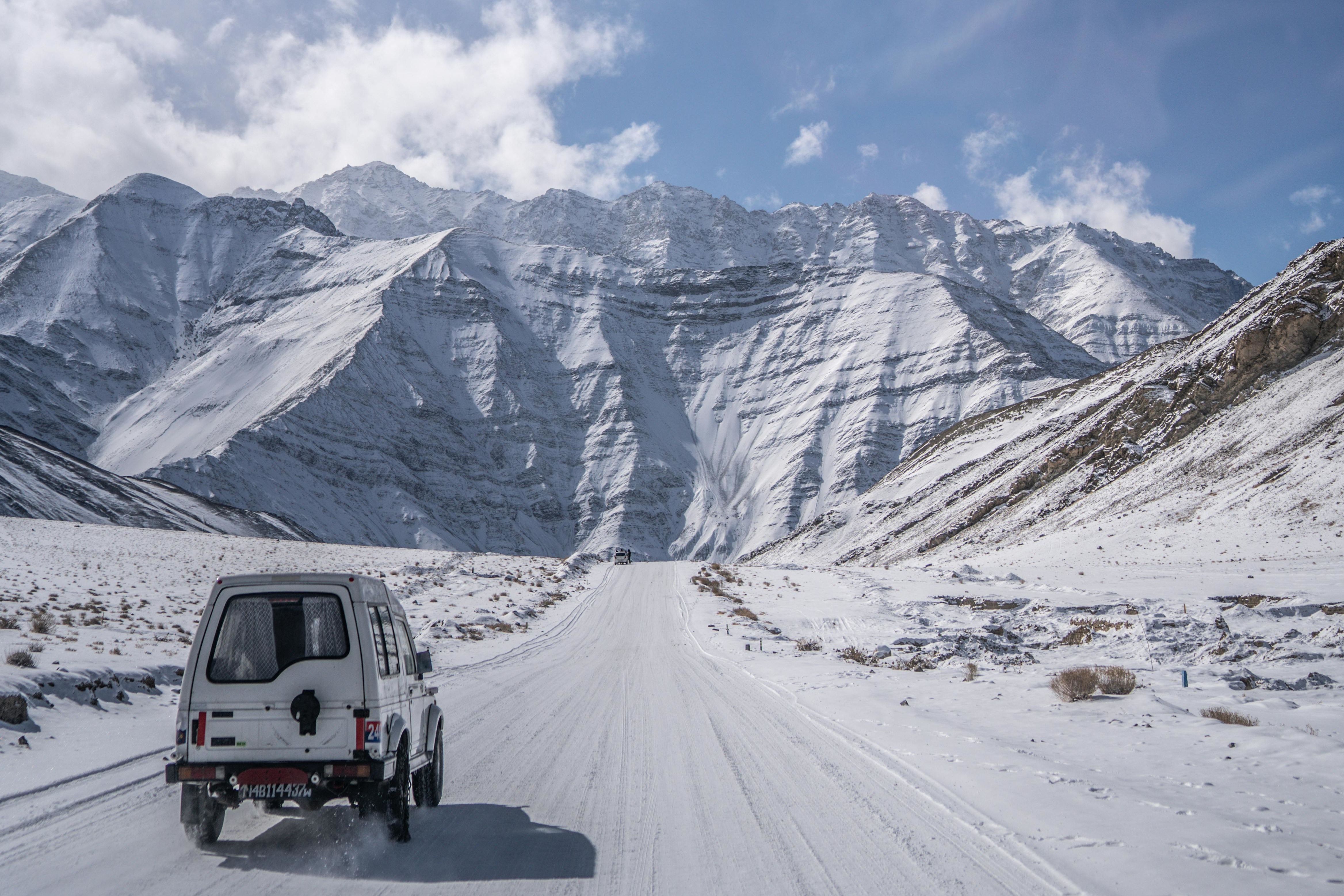 4X4 car on dirt road in snow near baralacha la pass with snow covered mountains in the background