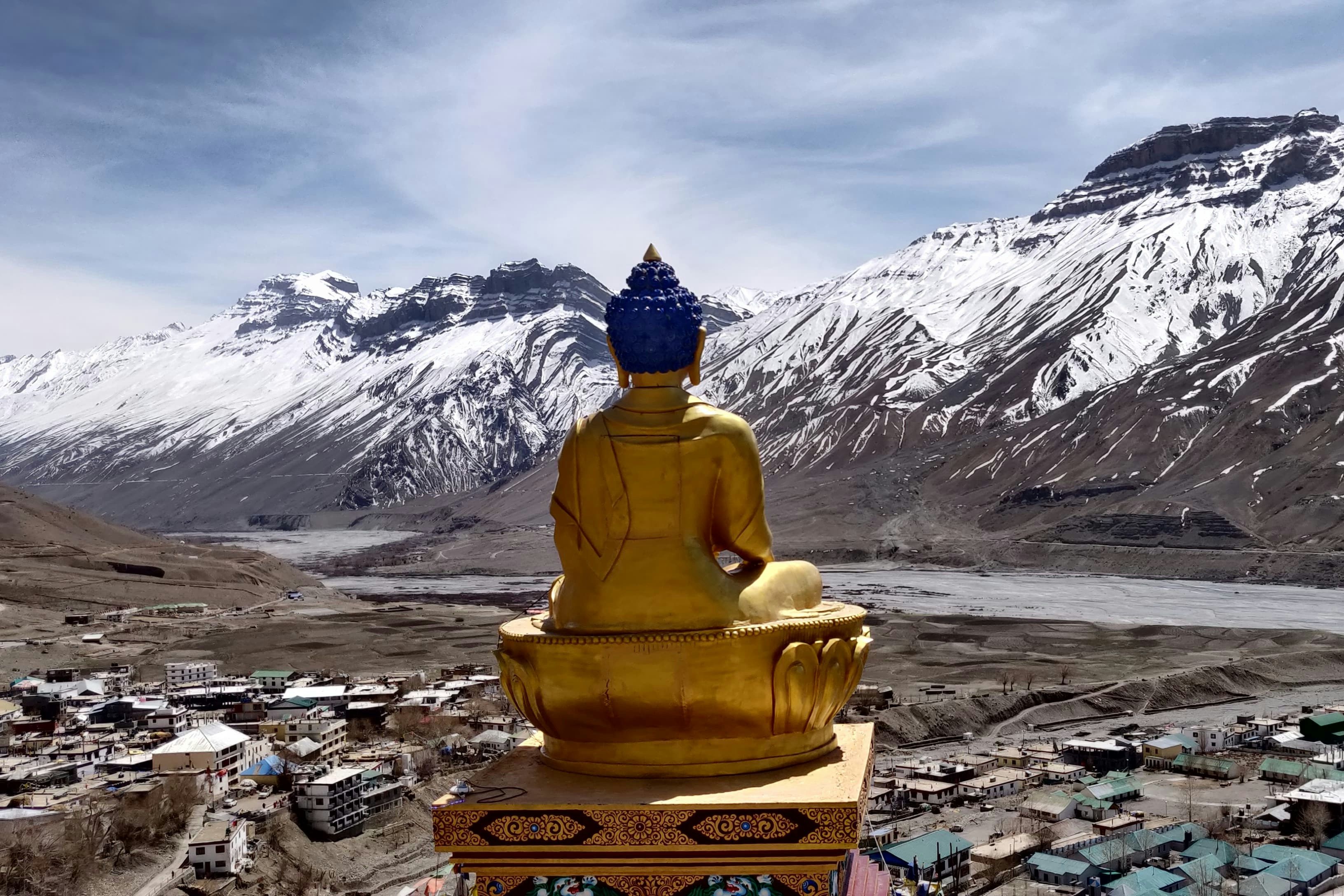 a golden statue of gautam buddha sitting on top of a hill in kaza village in spiti valley