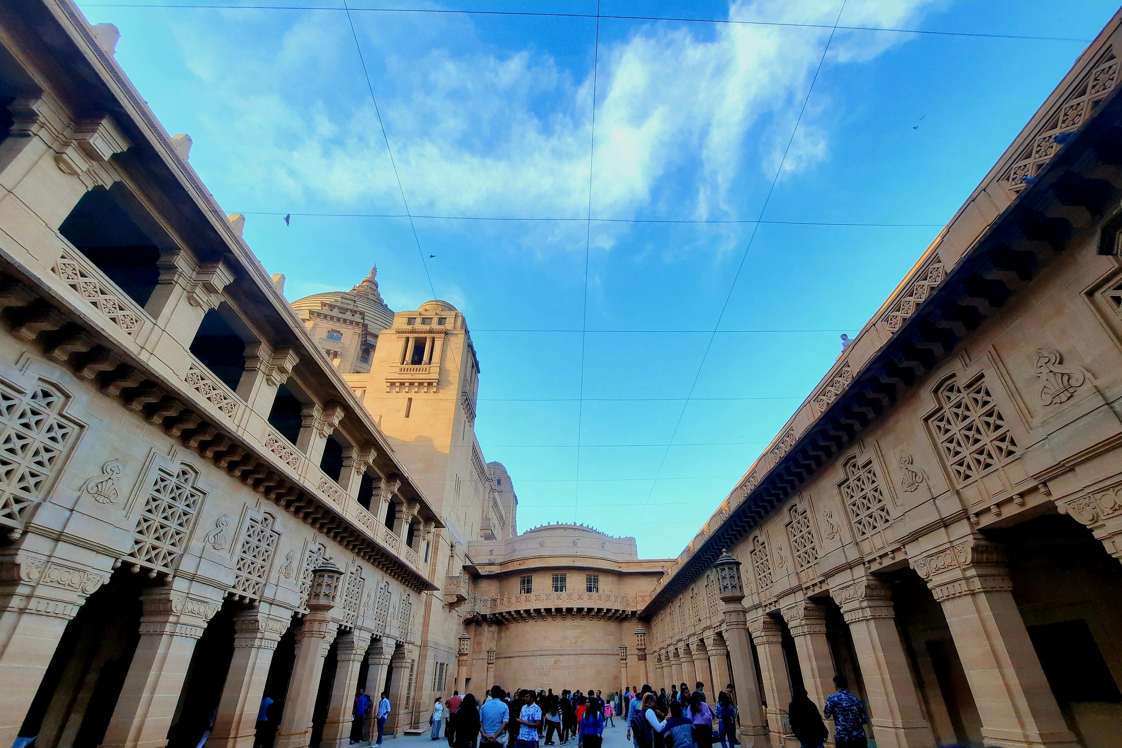 a group of people standing in a courtyard of umaid bhawan palace at jodhpur with clear blue sky