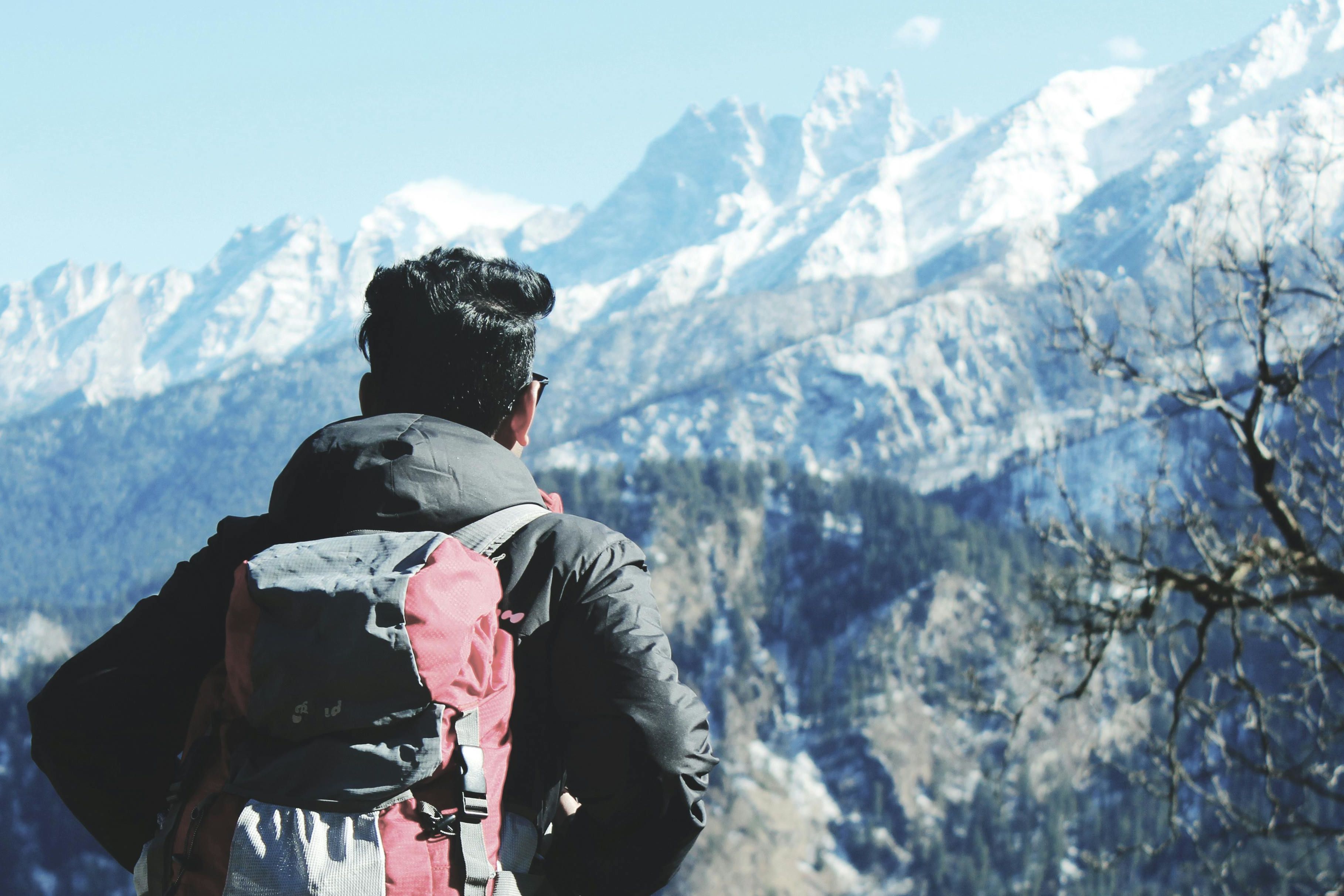a man in black hooded jacket and red backpack facing snow covered mountain