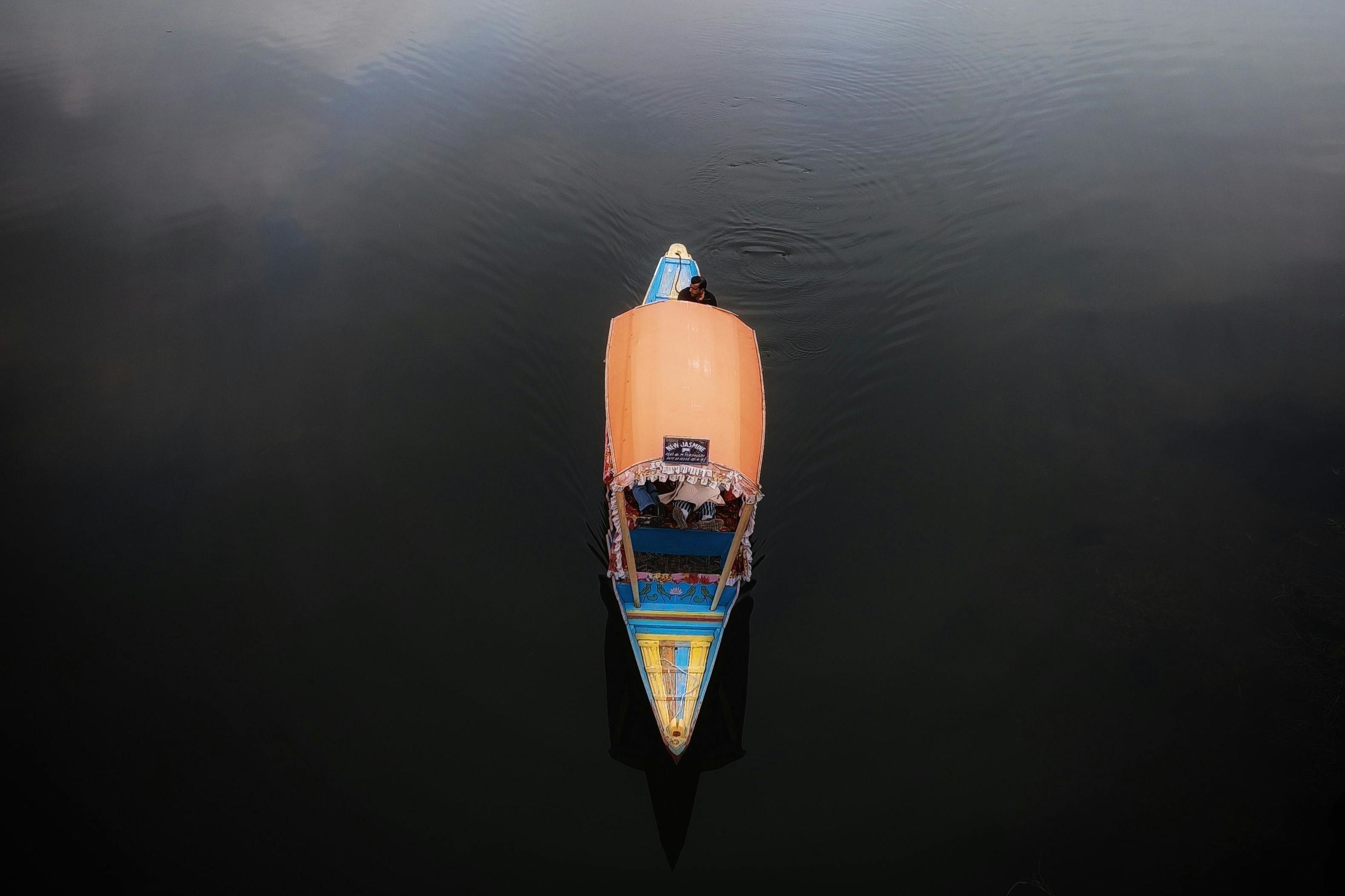a person in yellow and blue shikara sailing on calm water in dal lake