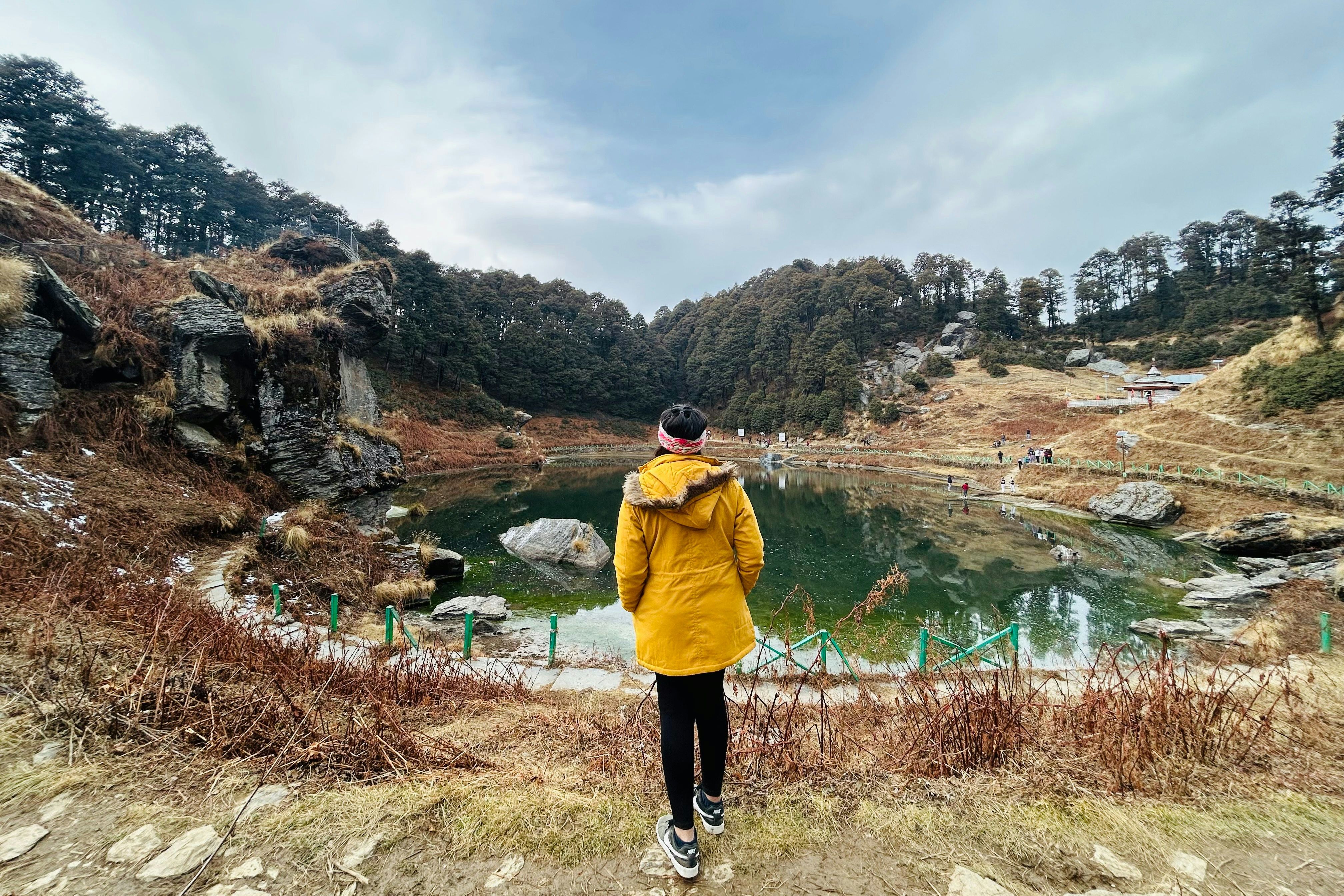 a person in a yellow jacket looking at a lake near jibhi