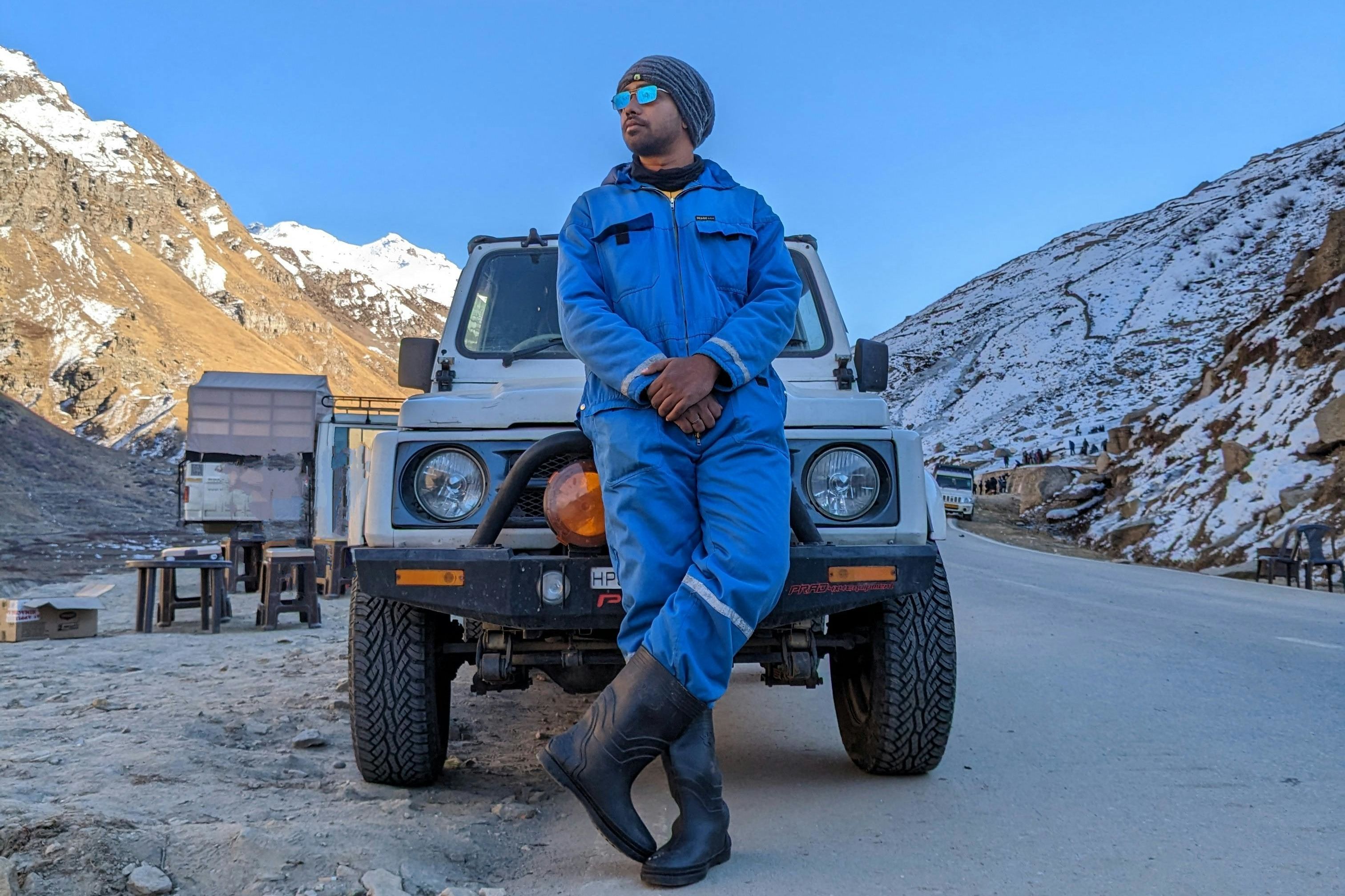 a person standing in front of a car parked on the side of a road in snowy mountains
