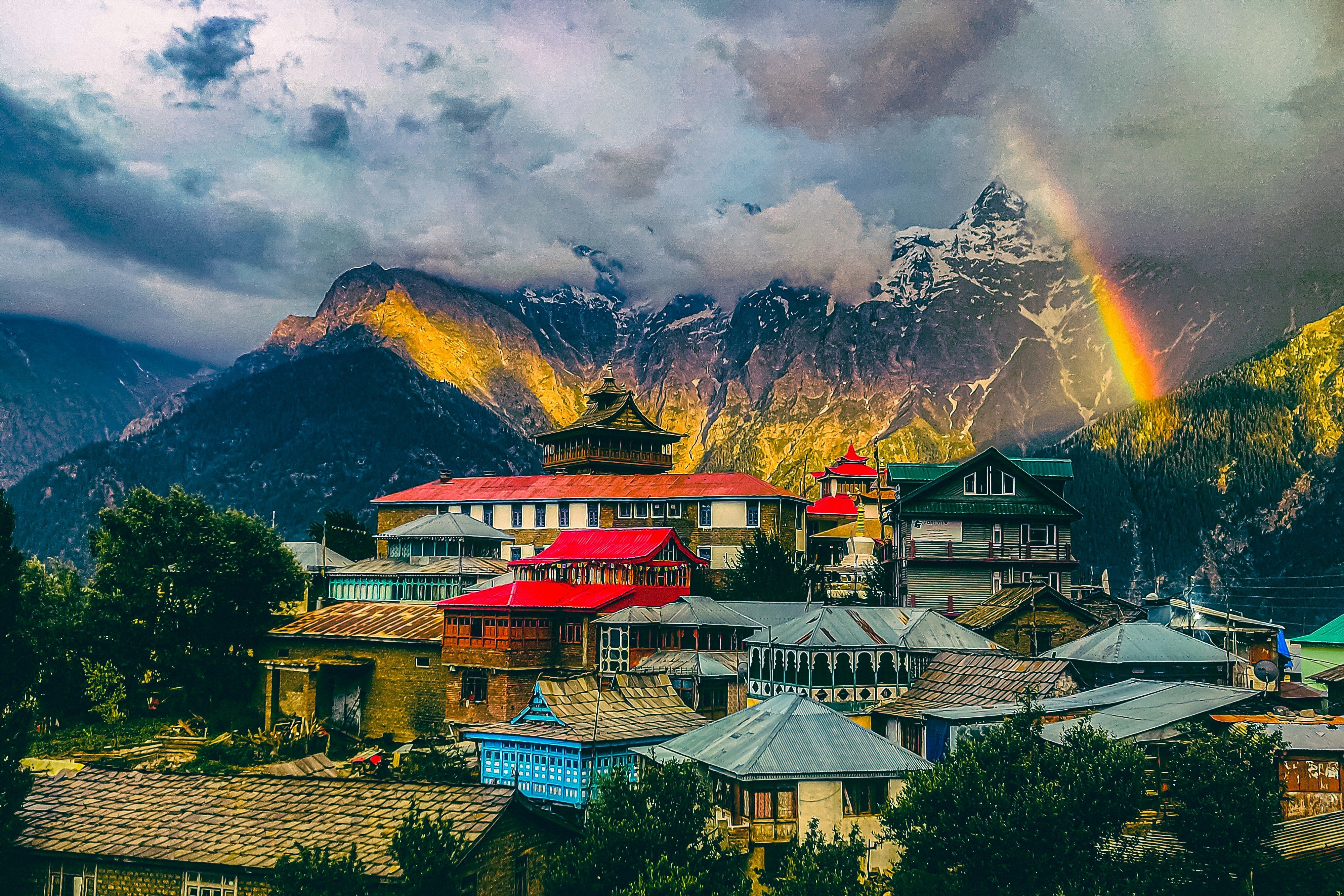 a rainbow shines in the sky over a mountain village in kalpa