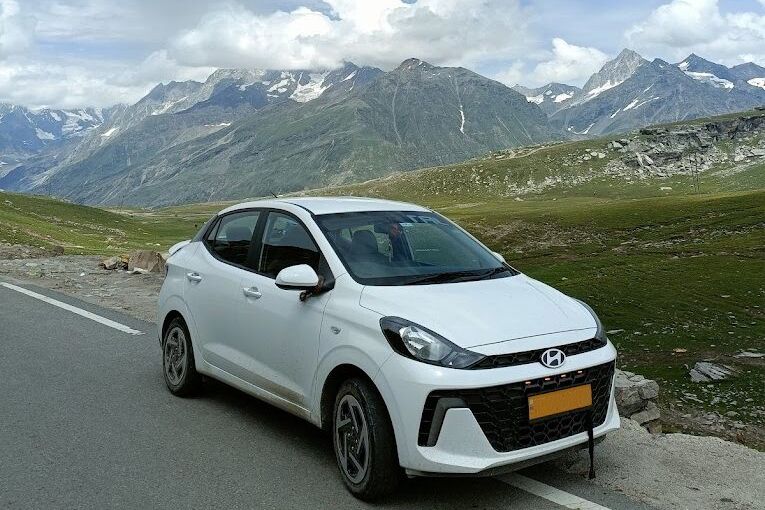 a sedan taxi standing on the side of a road in himachal pradesh with mountains in the backdrop
