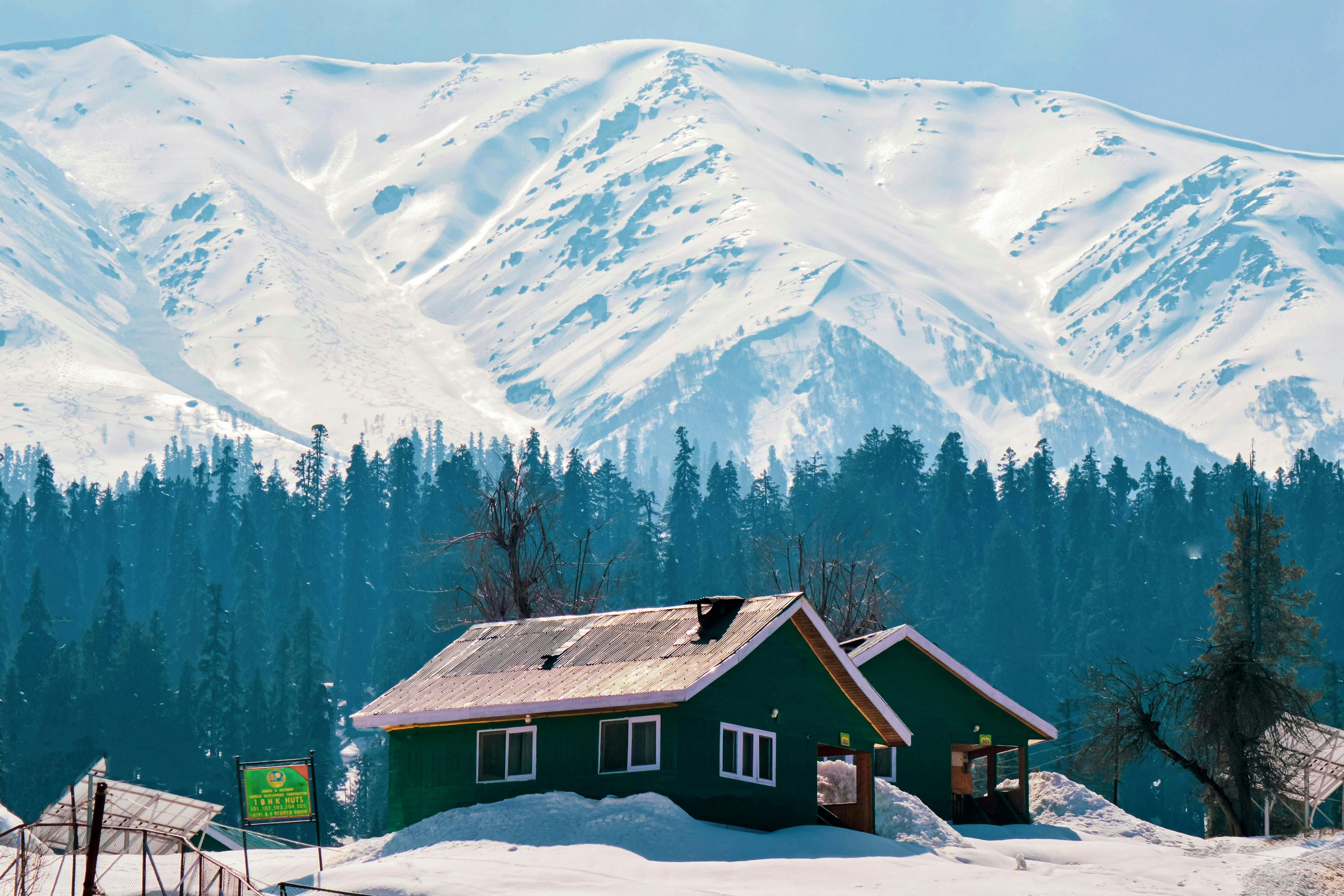 a small brown coloured house in gulmarg with snow covered mountains in the backdrop