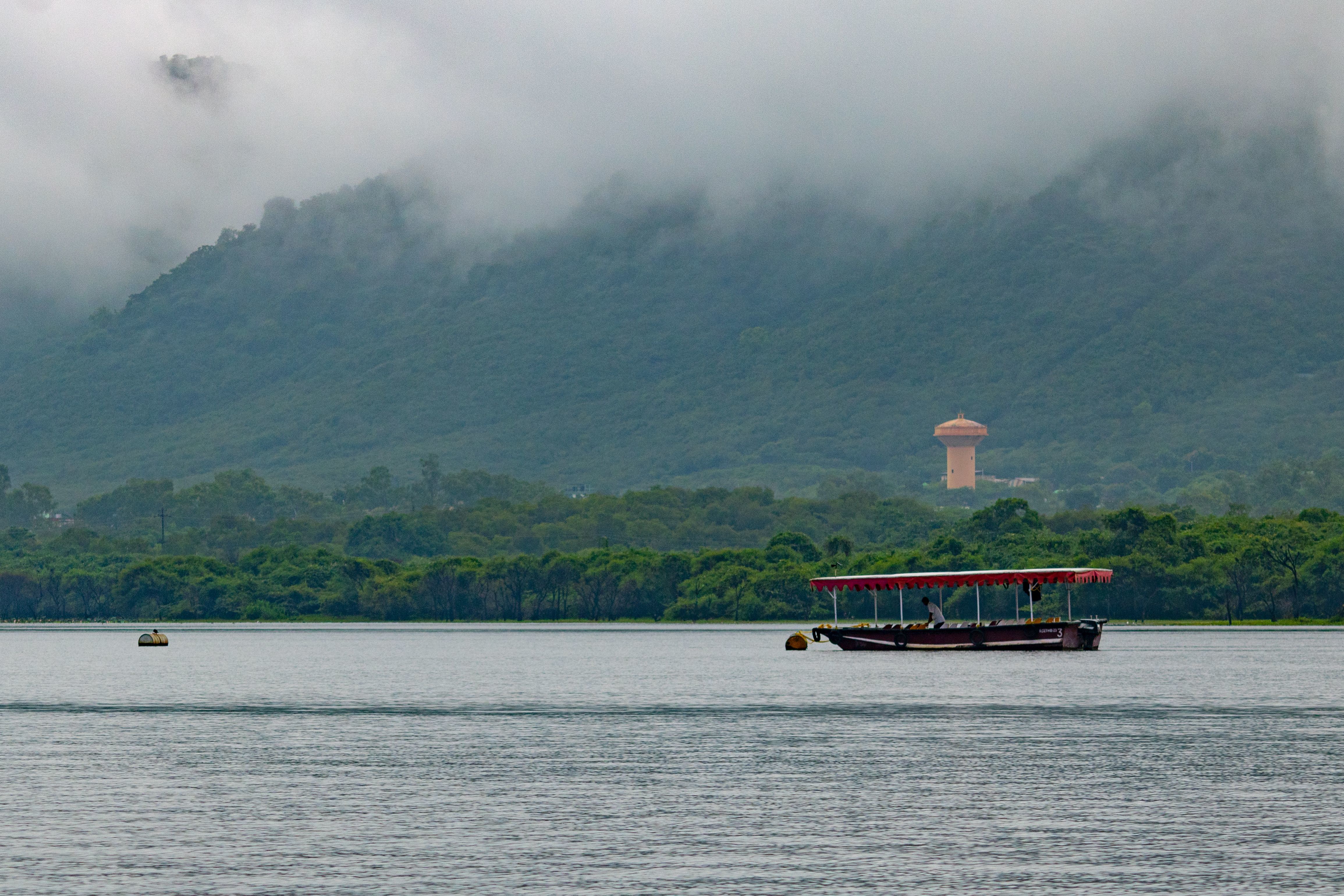a tranquil boat glides on fateh sagar lake surrounded by misty mountains in udaipur