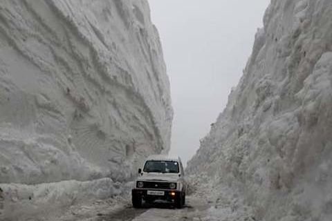 a vehicle passing through a narrow road near rohtang pass with snow walls on both sides