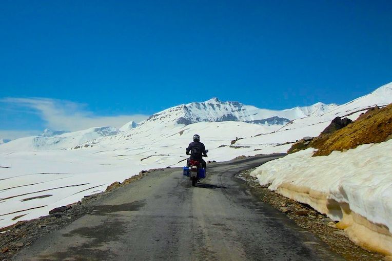 a person riding a motorcycle near baralacha la pass with snow on both sides of the road