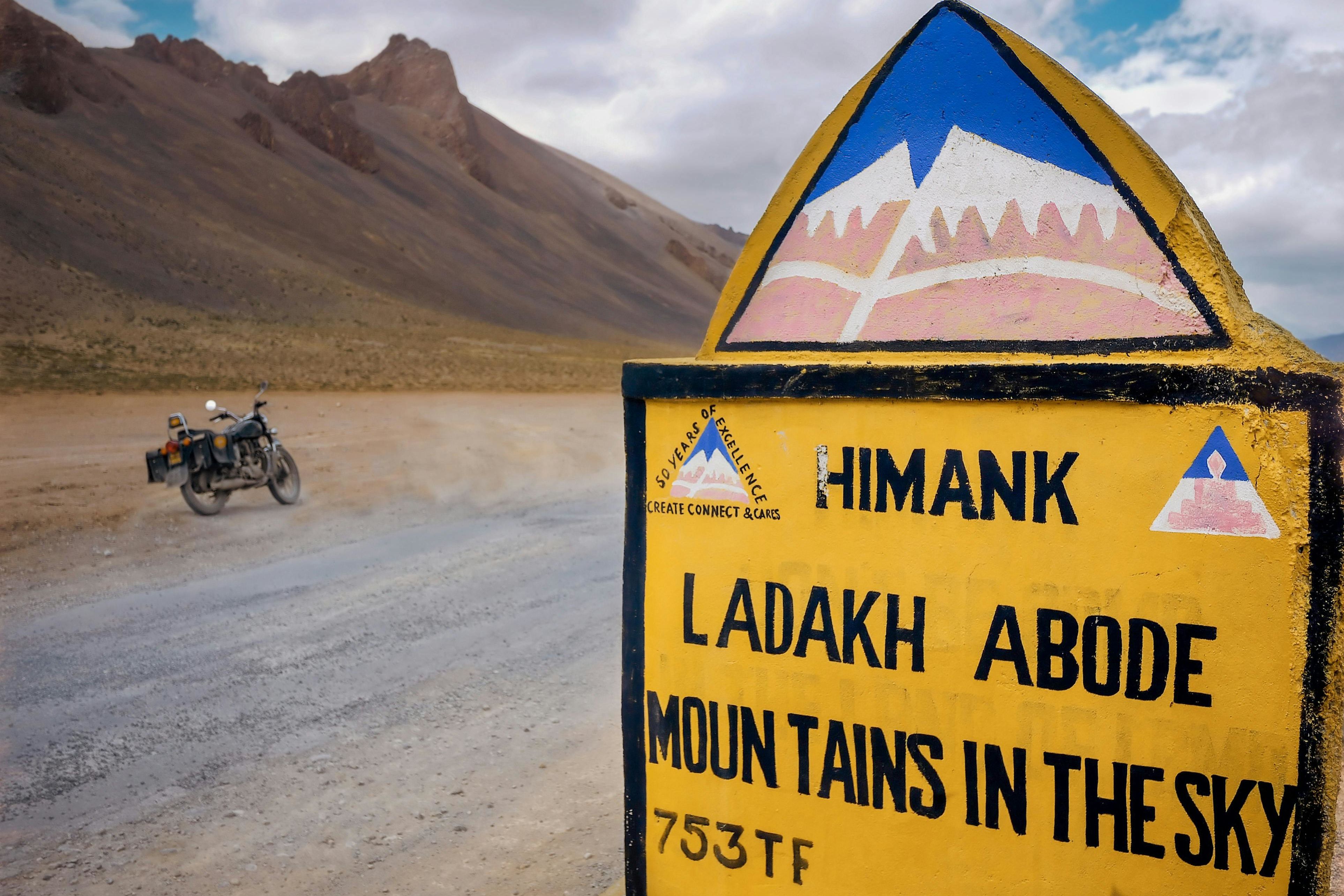 a motorcycle parked on gray and black sand near a road leading to ladakh