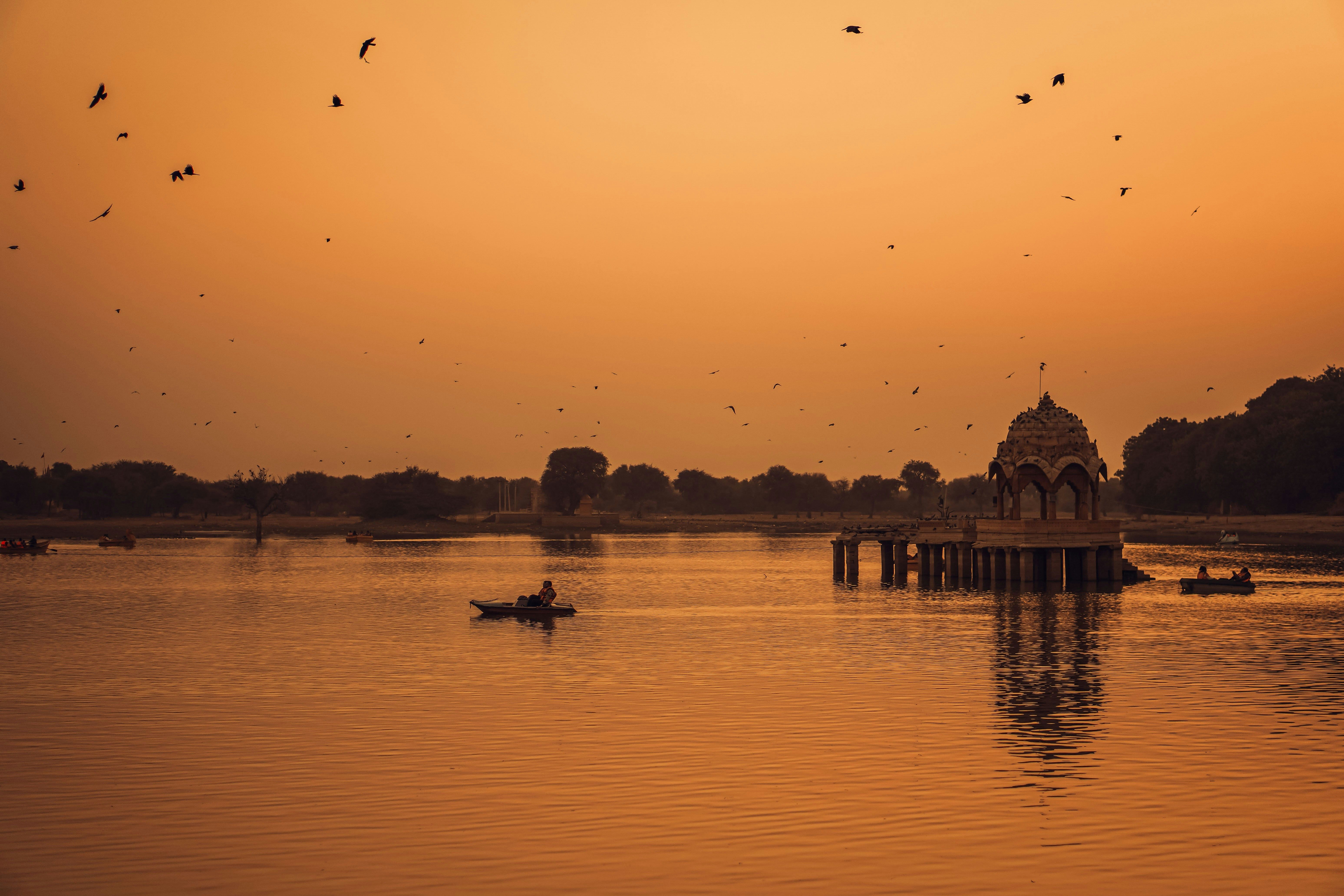 boats on the gadisar lake with a domed structure at sunset