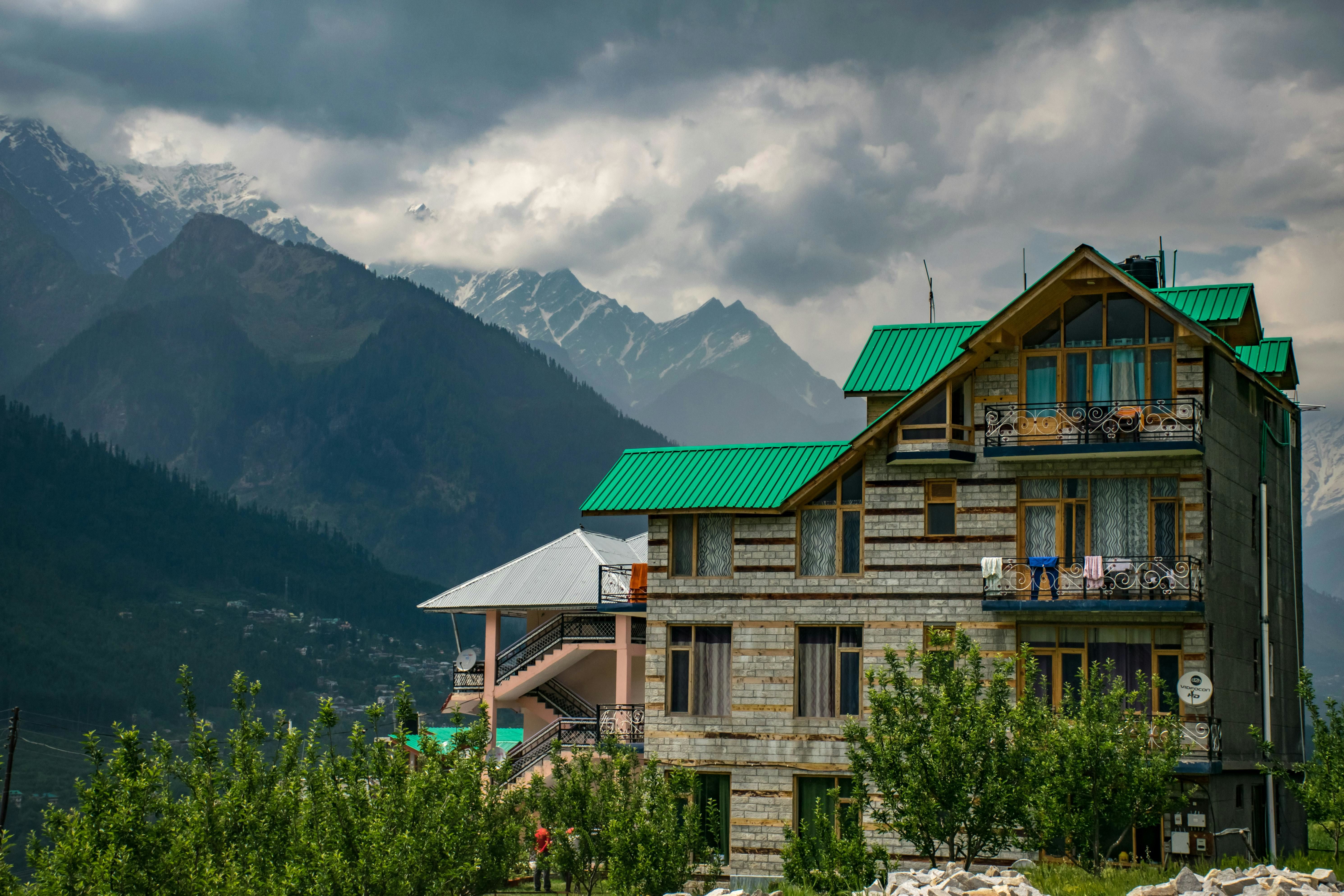 brown and green concrete building near a mountain on a cloudy day in manali