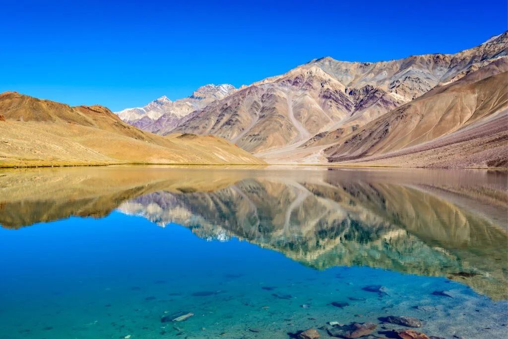 chandra taal lake surrounded by brown mountains during daytime
