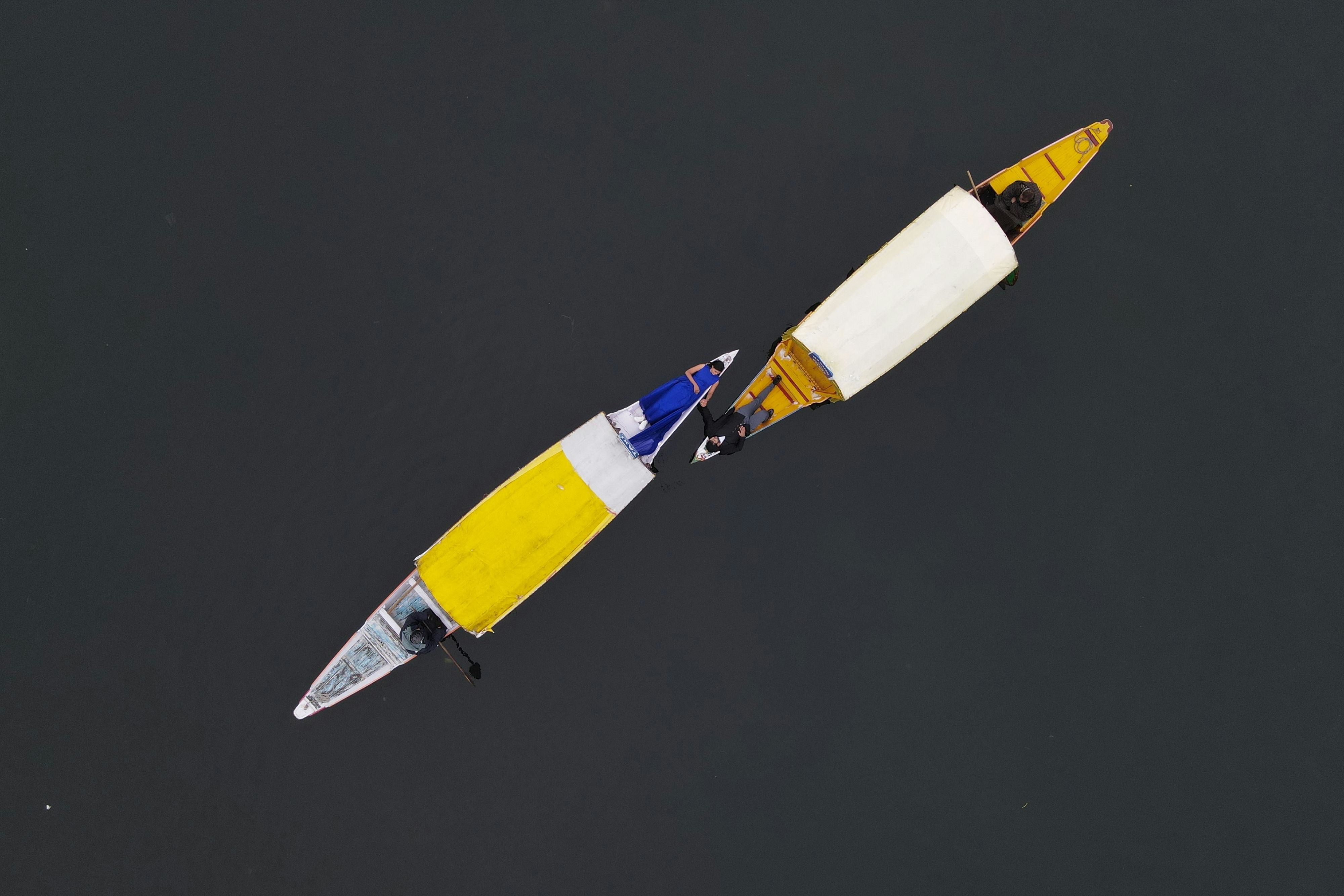 drone shot of a man and woman lying on separate shikara and holding hands