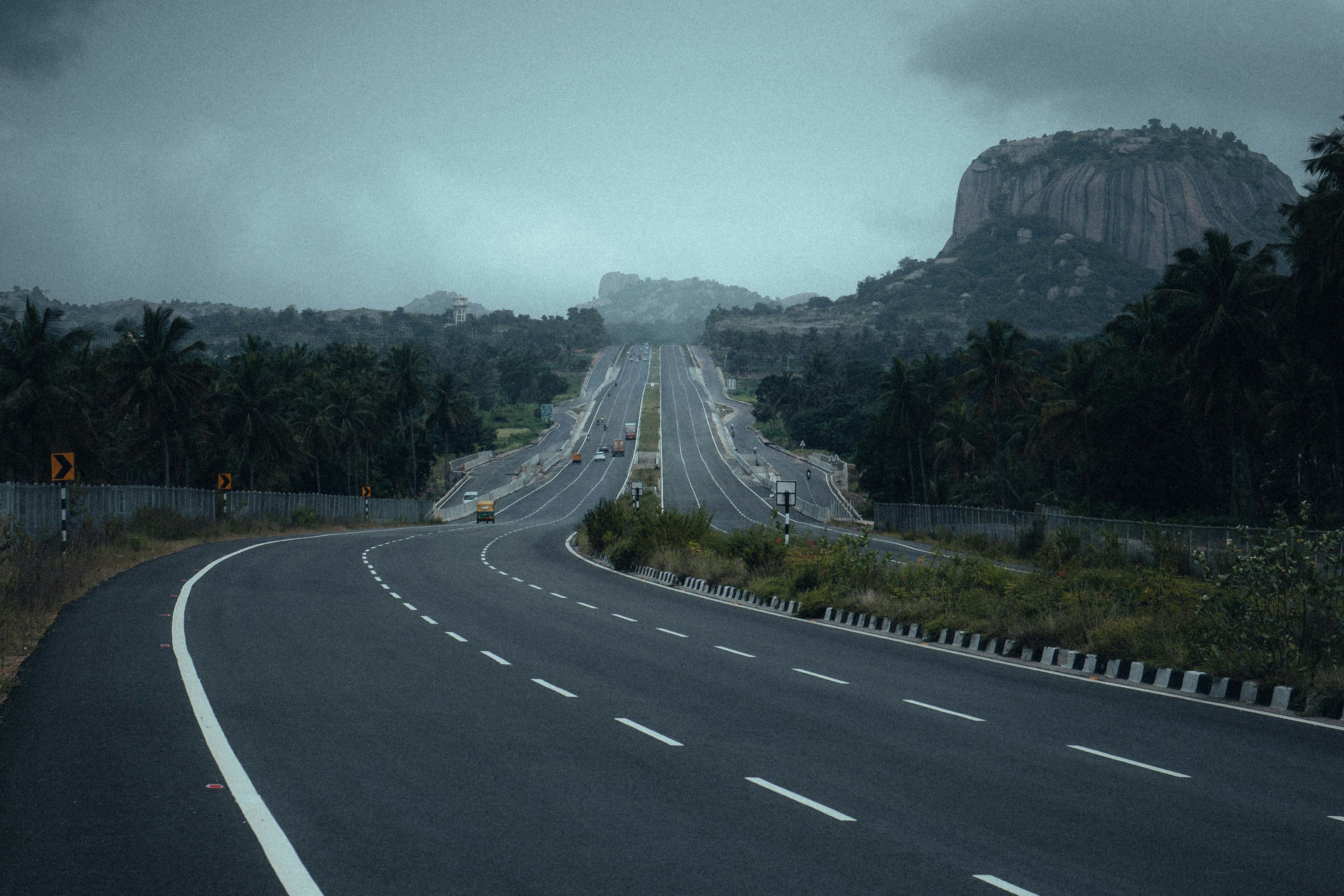 gray concrete road near green trees under dark cloud