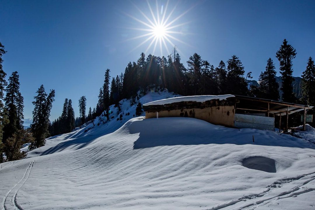 view of snow covered hatu peak in shimla with sun shining in the background