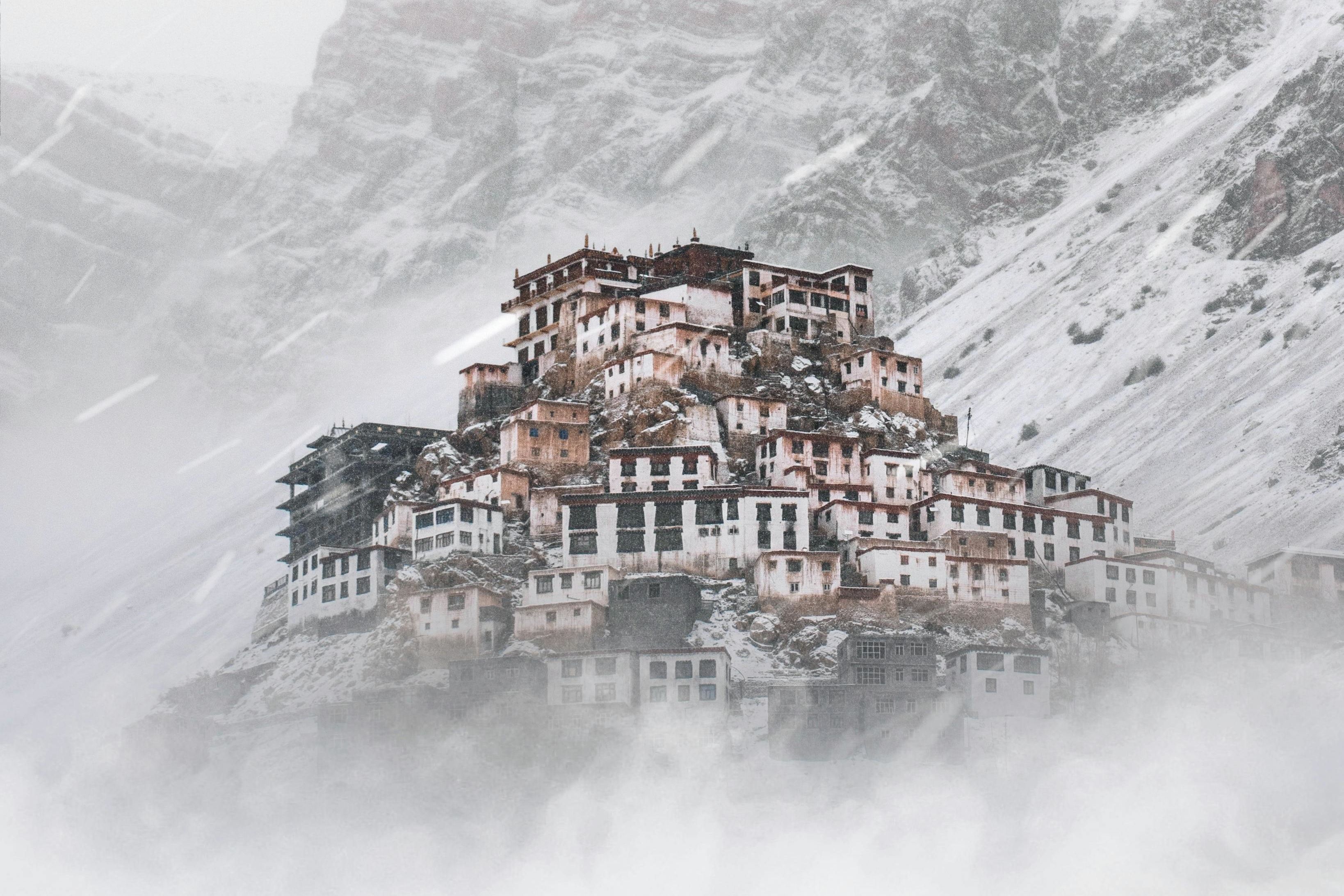 a view of key monastery during winter months with snow covered mountains in the backdrop
