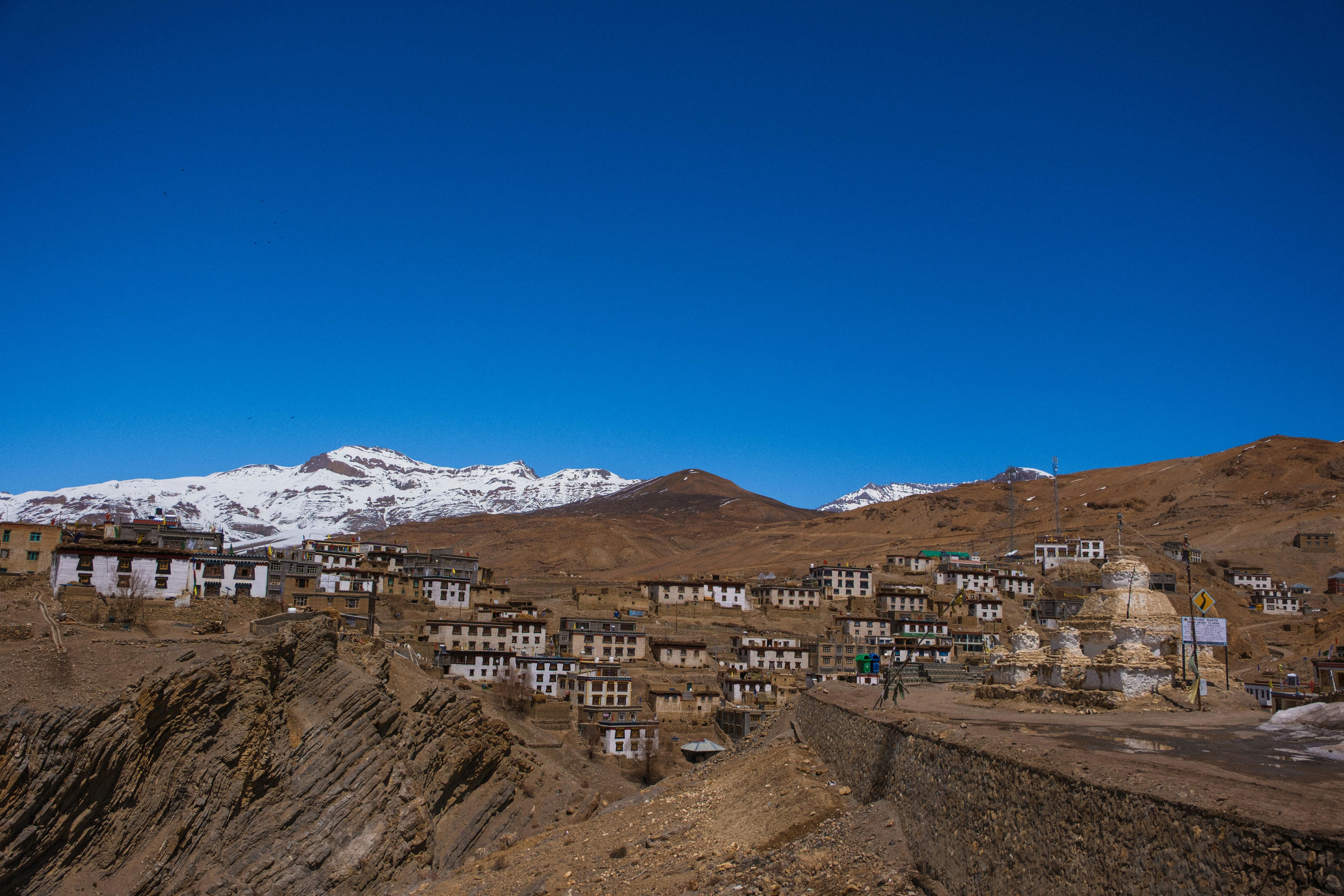 white and brown traditional houses in kibber village in spiti valley with snow capped peaks in the backdrop