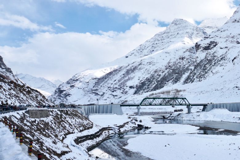 a river passing through lahaul valley with snow covered mountains in the backdrop