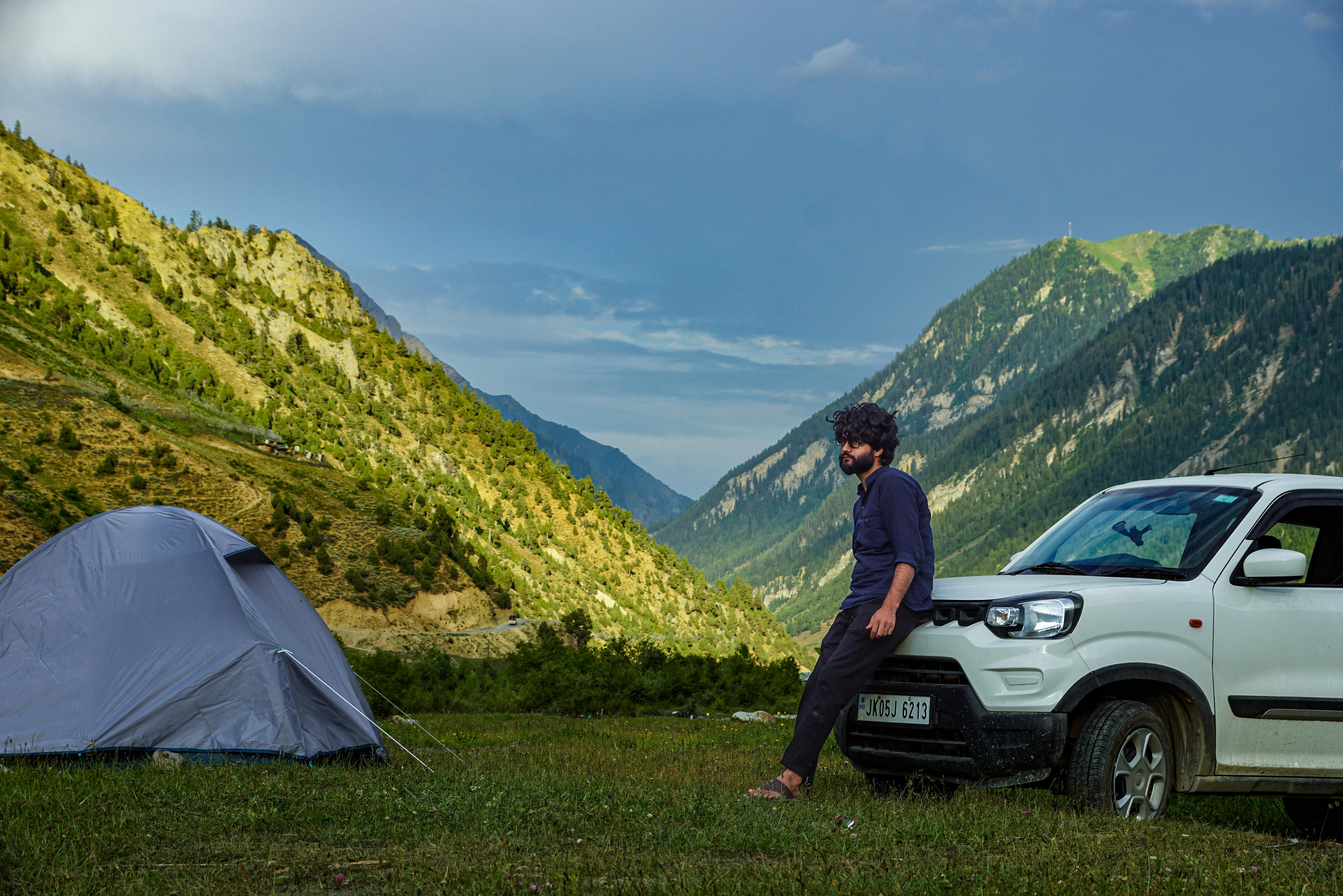a person leaning on a white car near gurez valley in kashmir