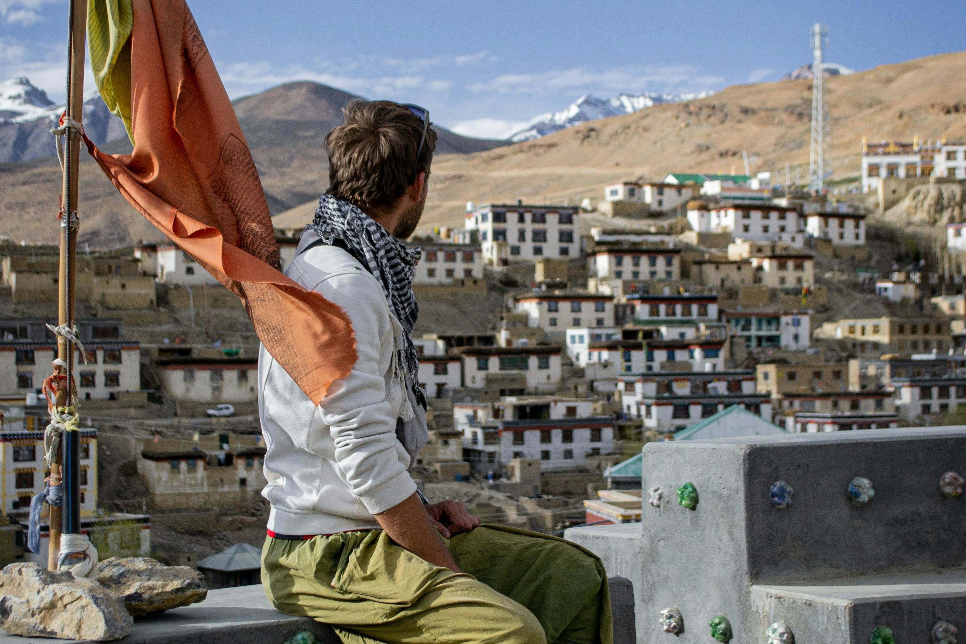 a man sitting on wall with flag and with town buildings behind him