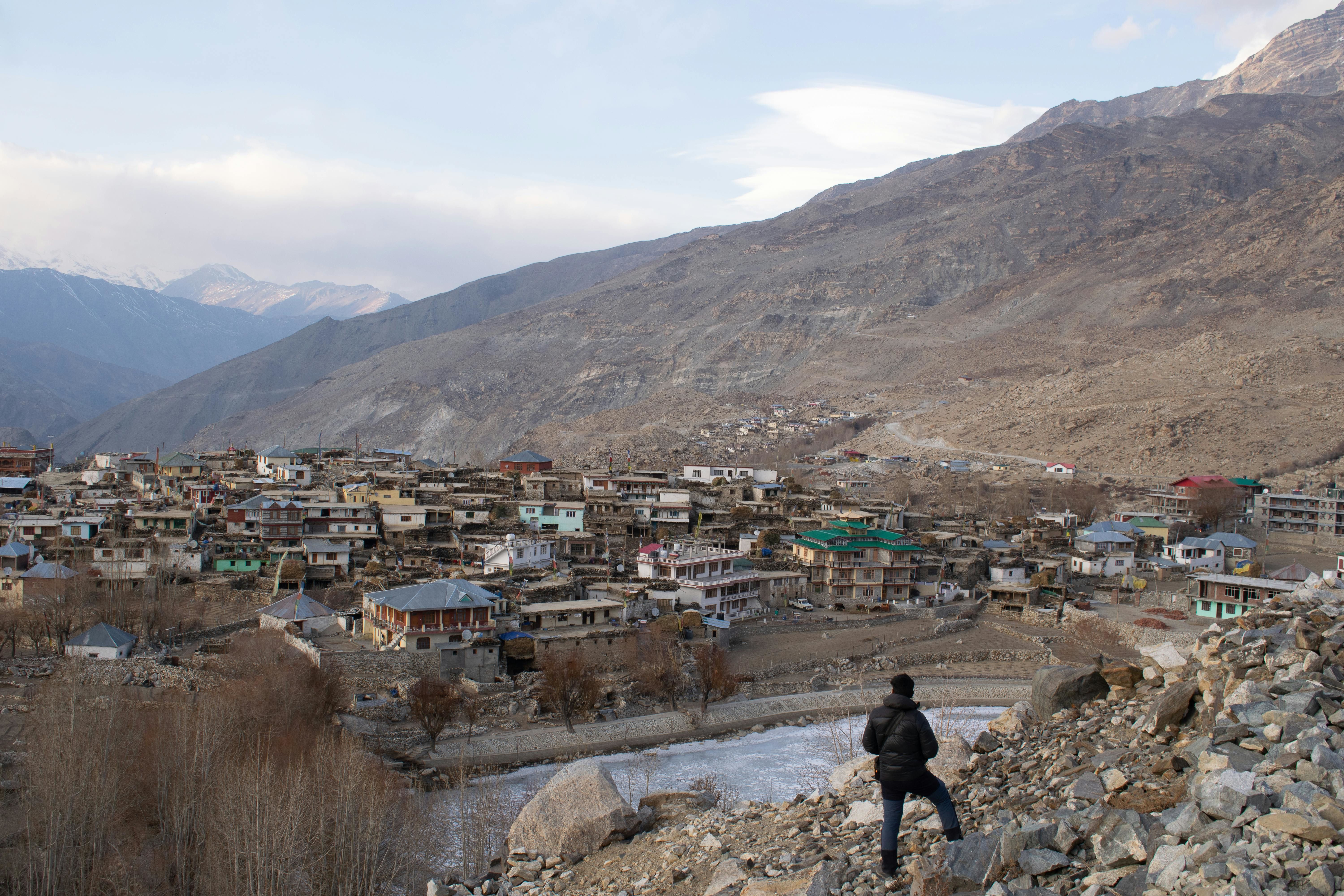 man standing on rocks over nako lake near nako village