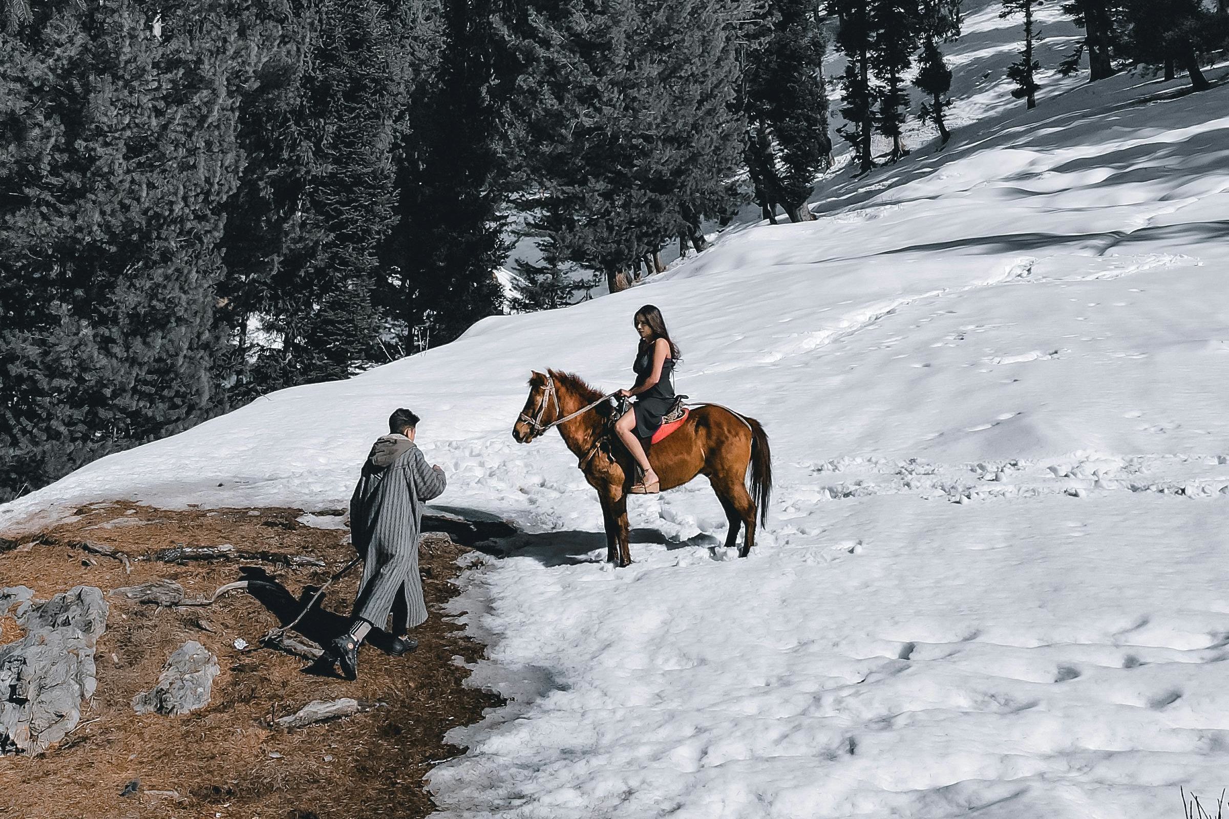 man walking towards a woman on a horse in snow near pahalgam