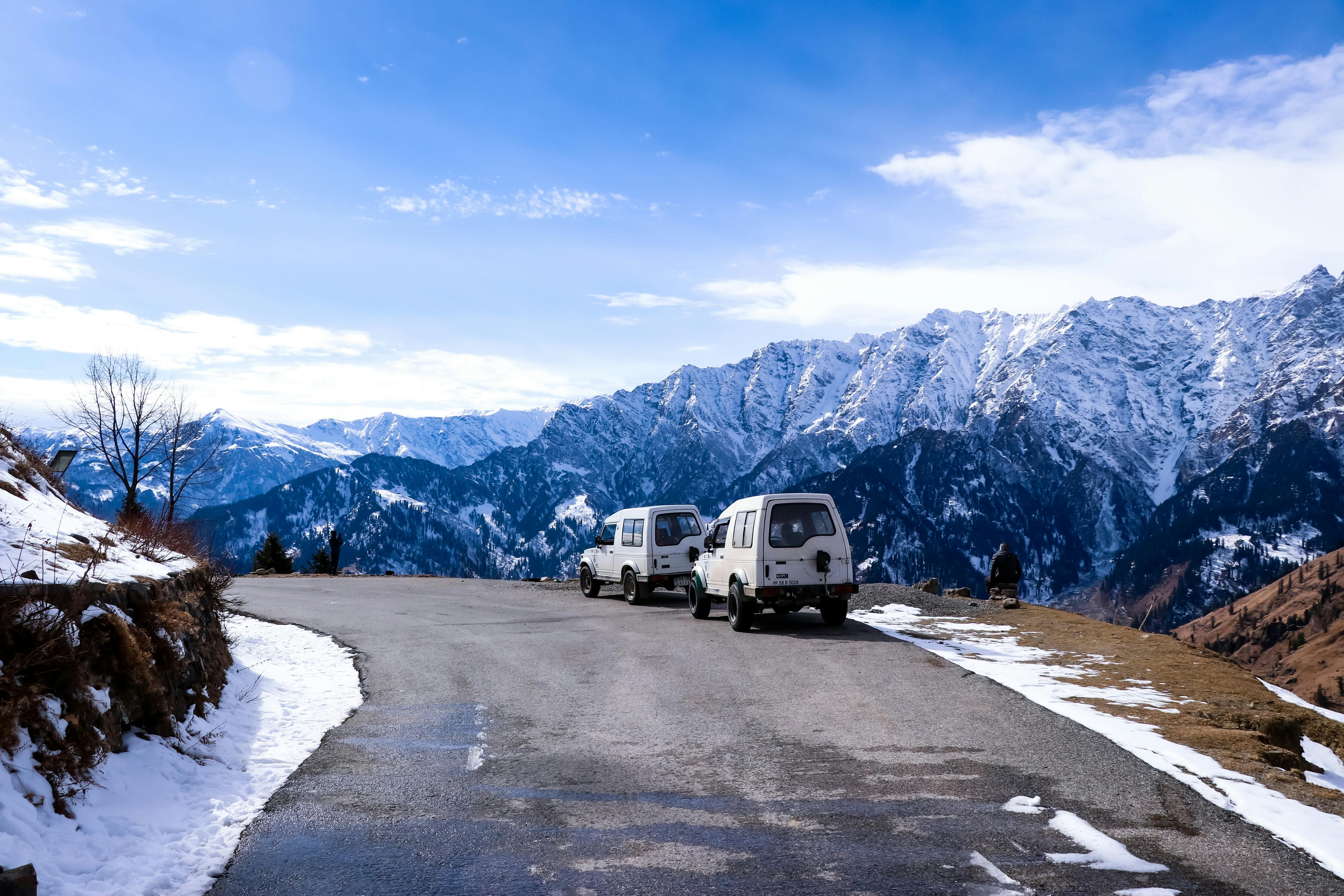 vehicles standing on a road with snow covered mountains in the backdrop