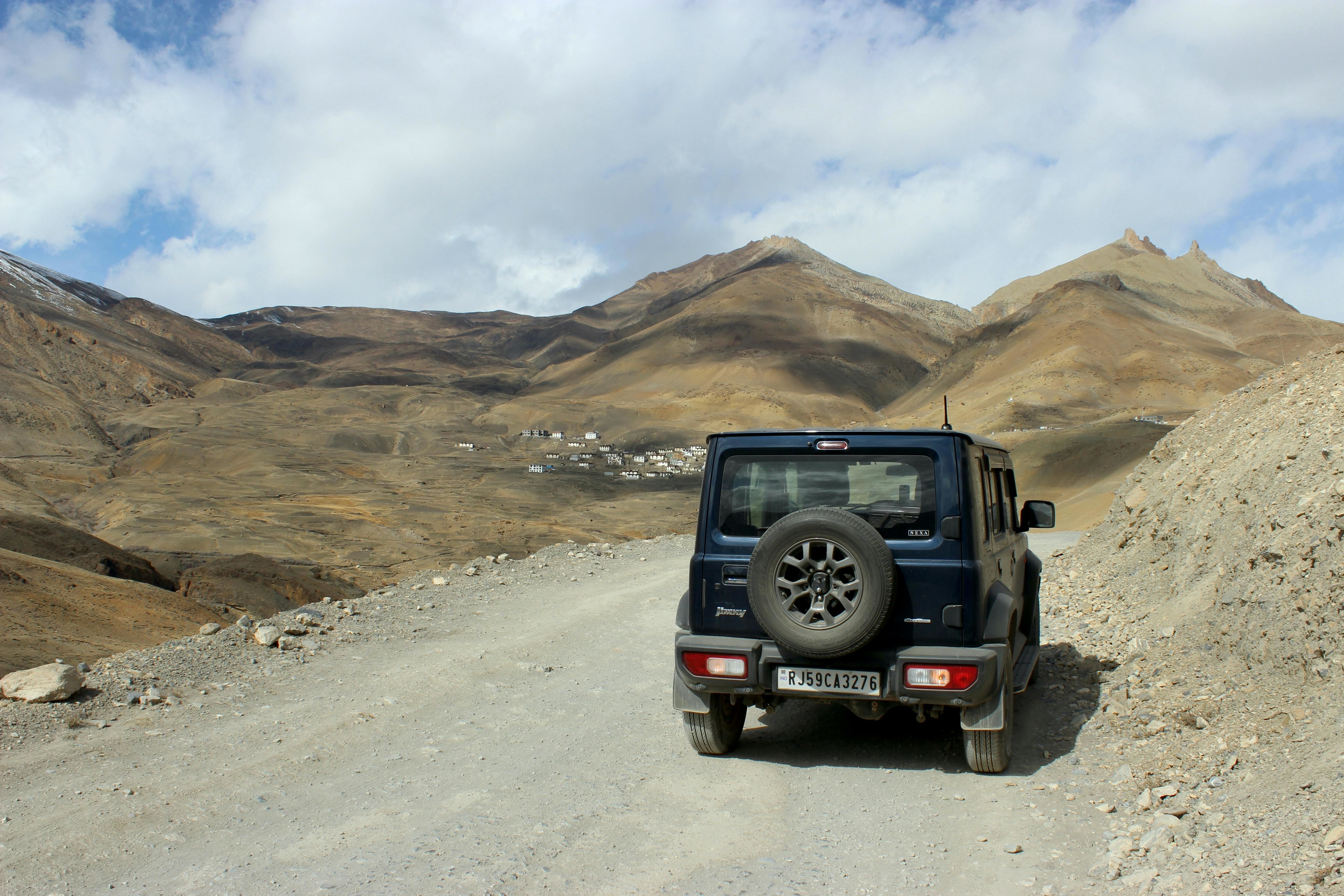 a car standing on a dirt road in spiti valley with brown mountins in the background