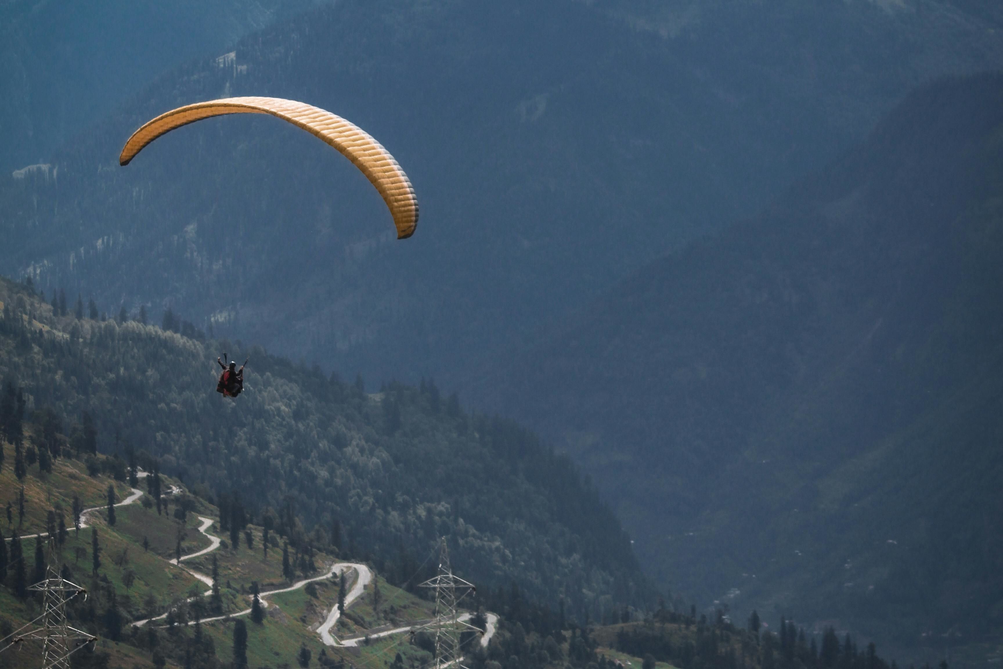 person riding yellow parachute over mountain range near manali