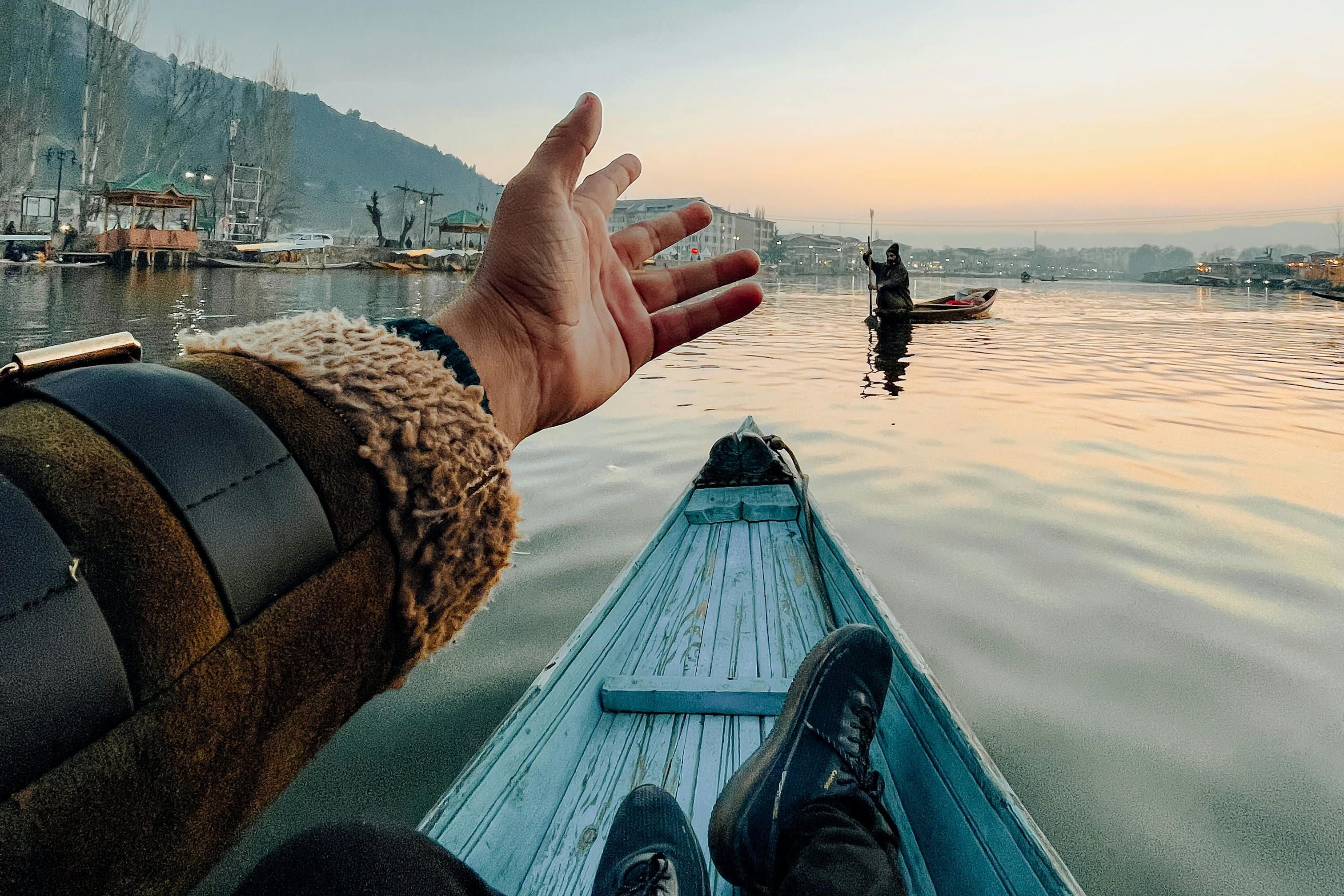 a person sitting with hand raised in boat at sunset