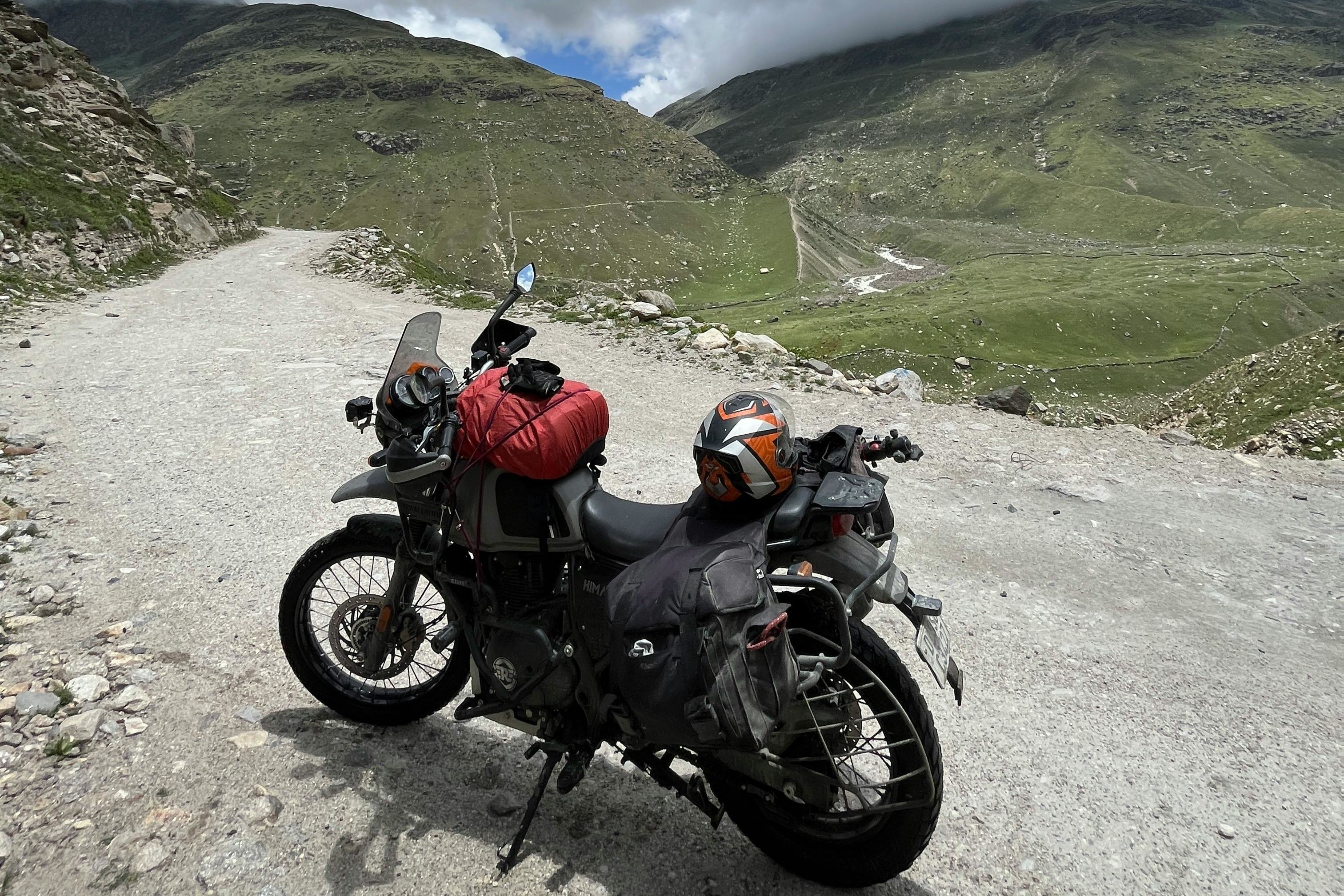 red and black motorcycle on green grass field under white clouds and blue sky in himachal pradesh