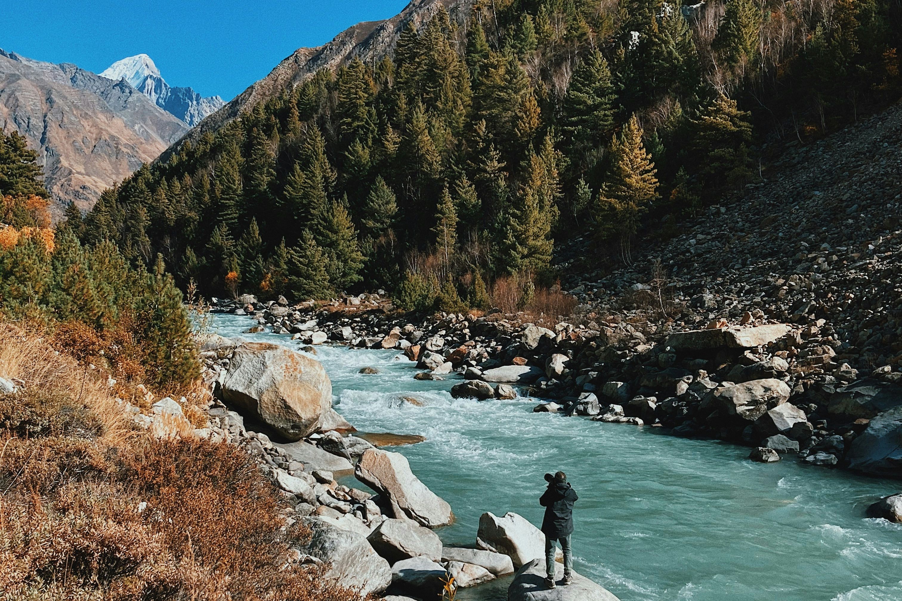 a person standing near a flowing river in kinnaur valley