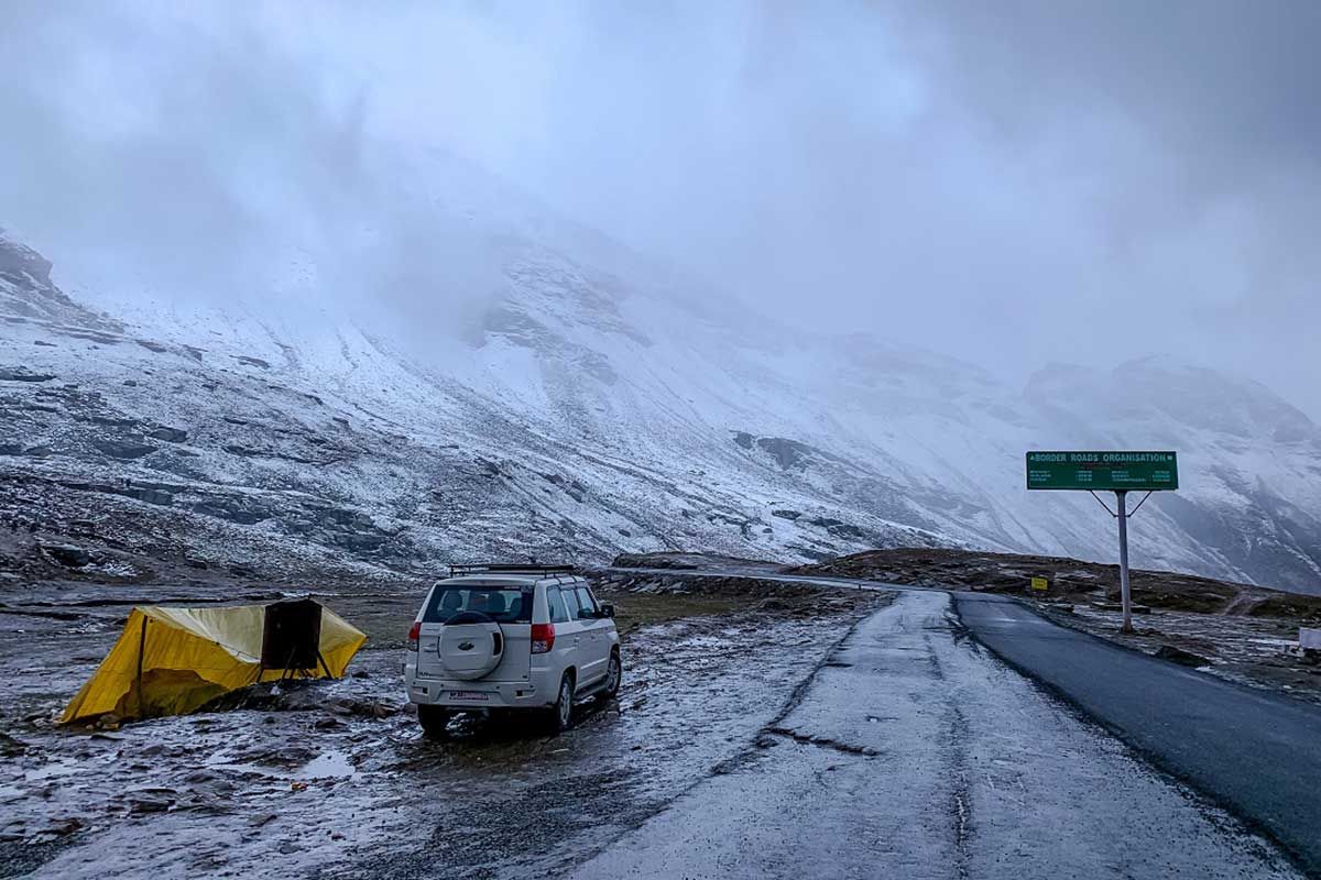 a vechicle standing beside a road with snow covered mountains in the backdrop on a cloudy day