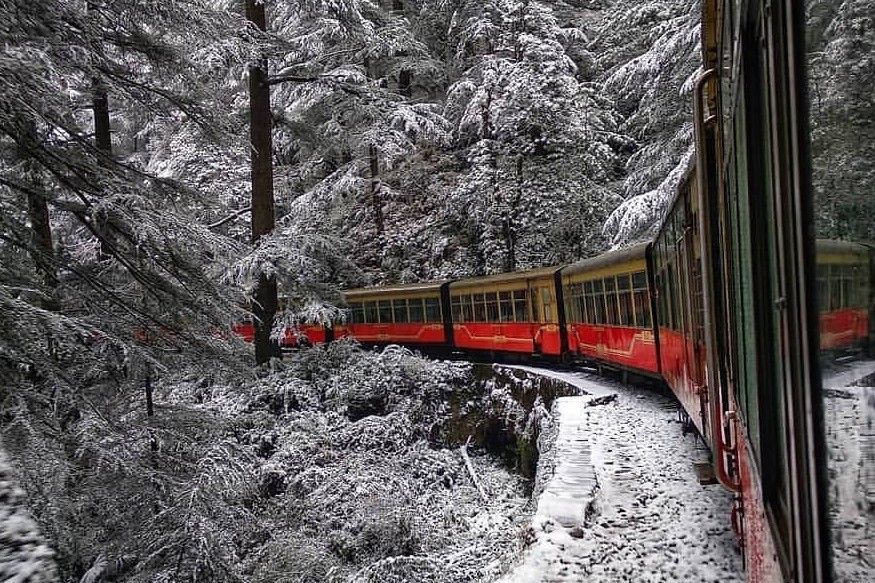 toy train passing through mountains and snow covered pine trees