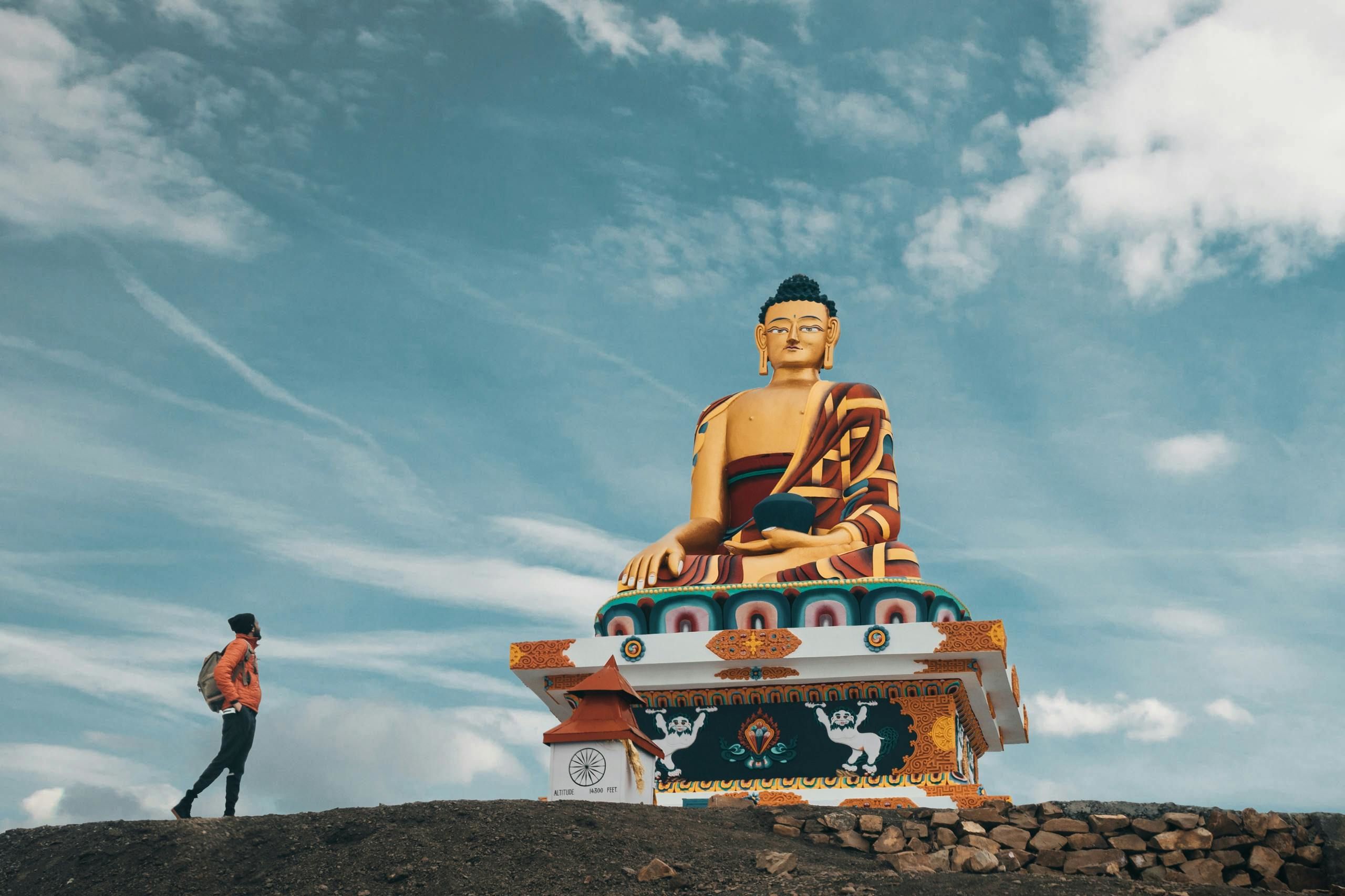 a traveler standing near a giant buddha statue located in mountainous valley