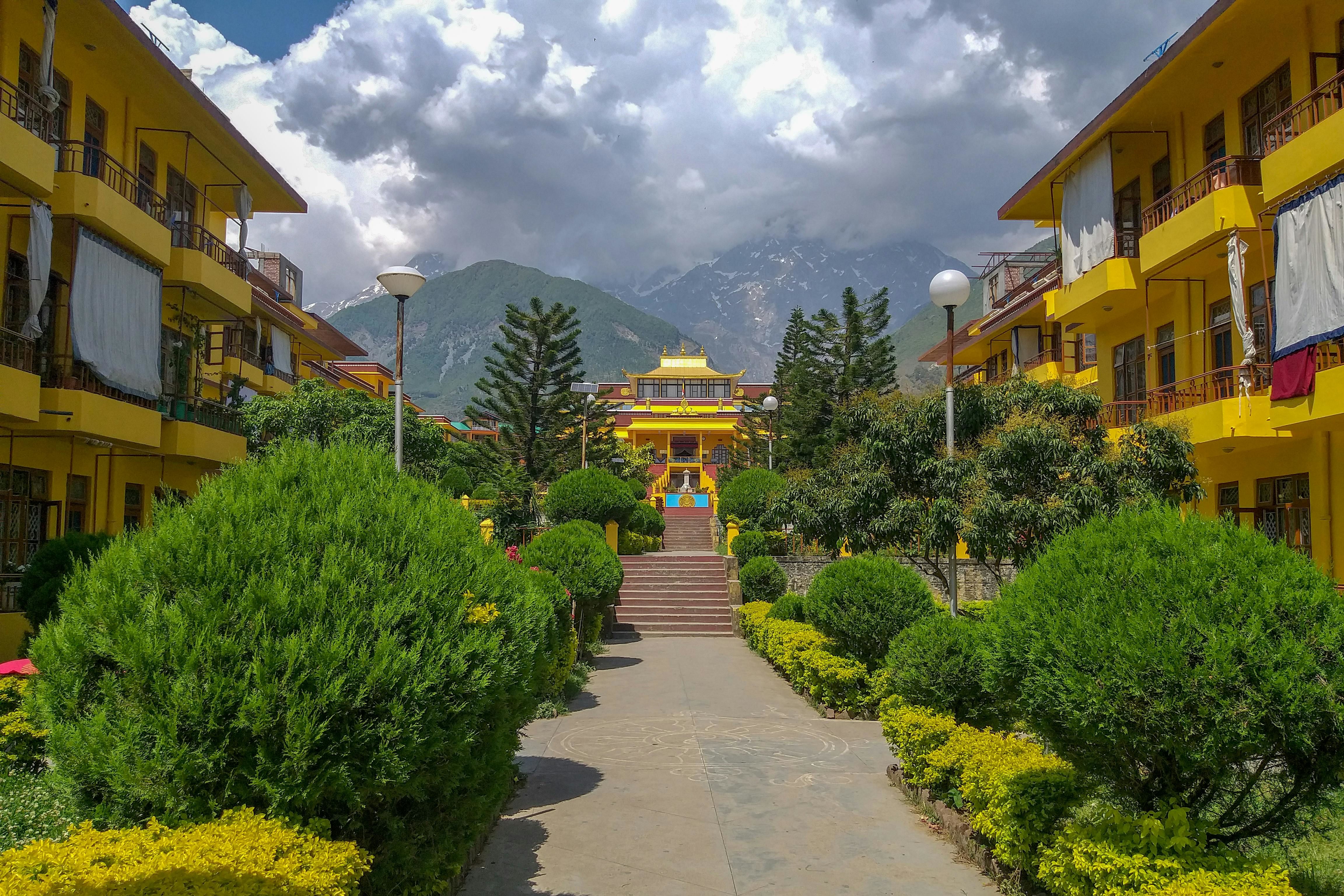 a view of tsuglagkhang monastery in dharamshala with cloudy sky and mountains in the backdrop
