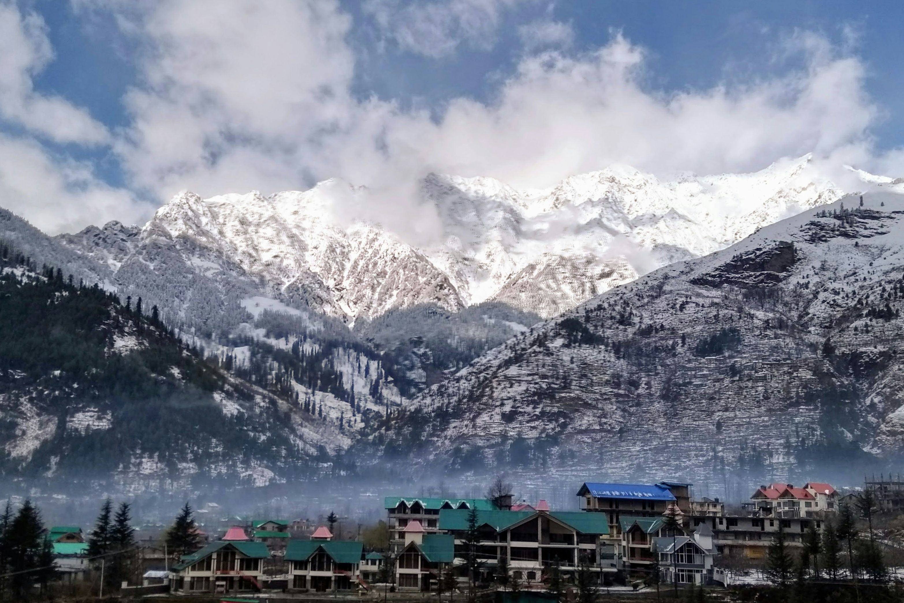 view of houses in manali with snow covered mountains in the background