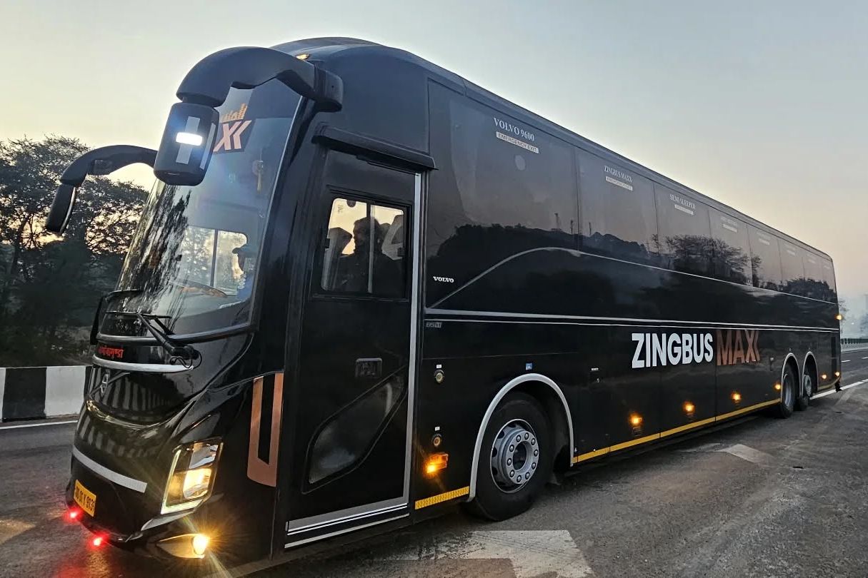 a black volvo bus on road travelling between delhi and manali