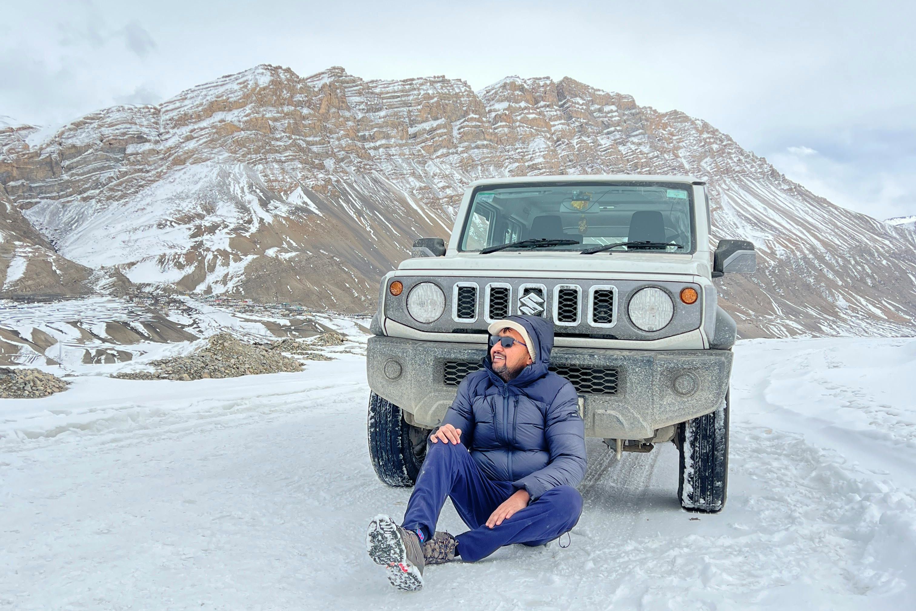 a person sitting in front of a car with white snow around