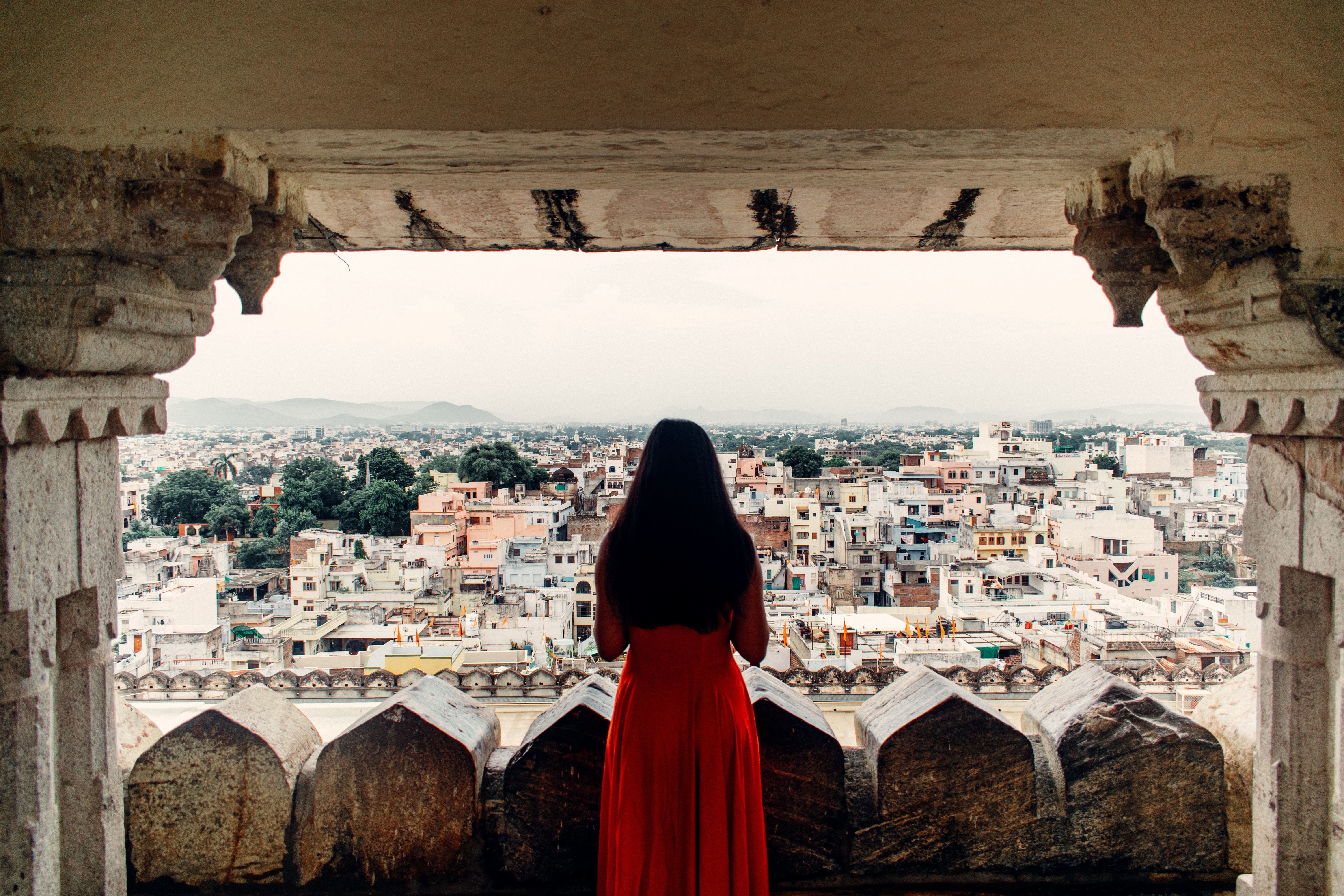 woman in red dress observing udaipur cityscape from a balcony