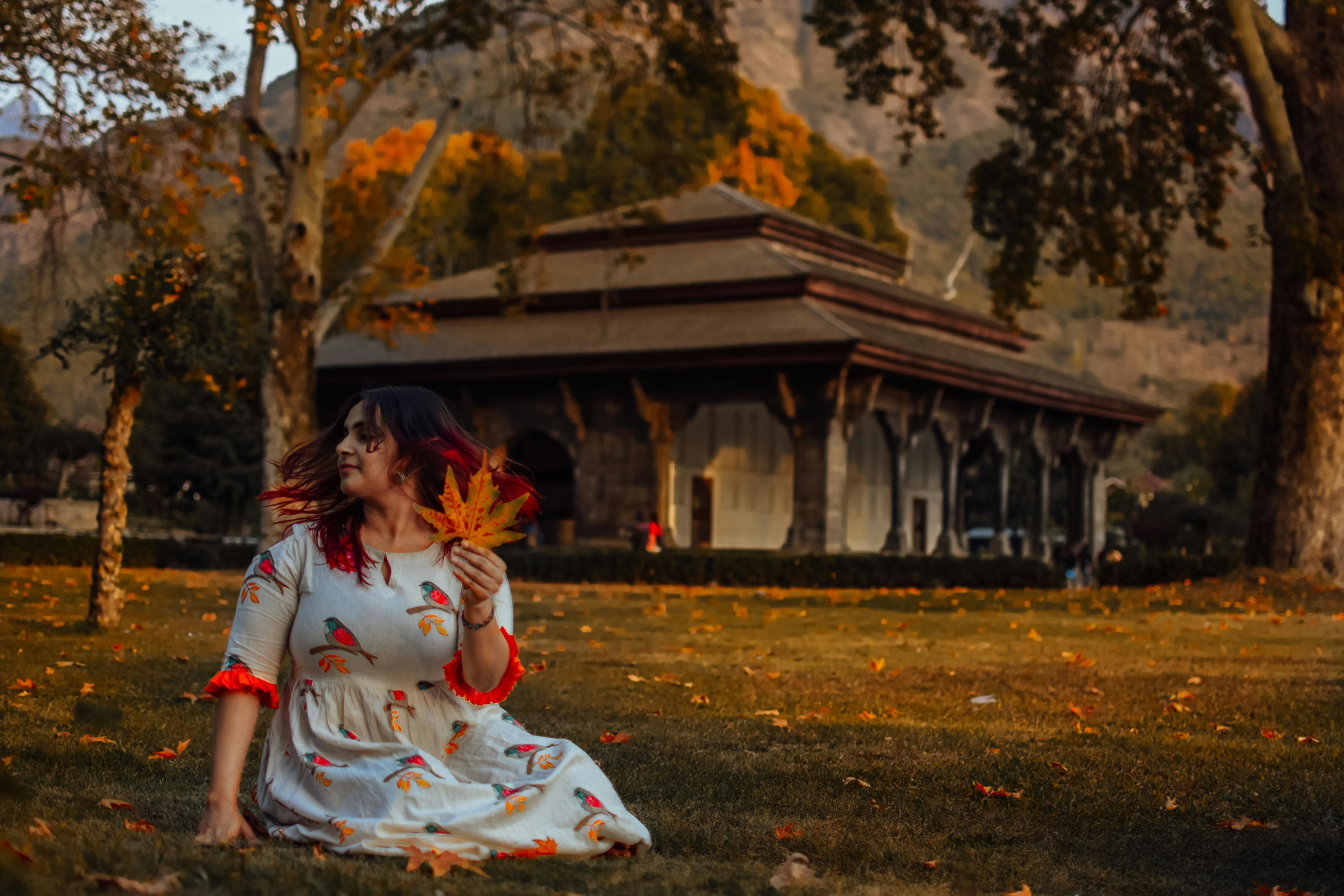 a woman in white and red floral dress holding maple leaf